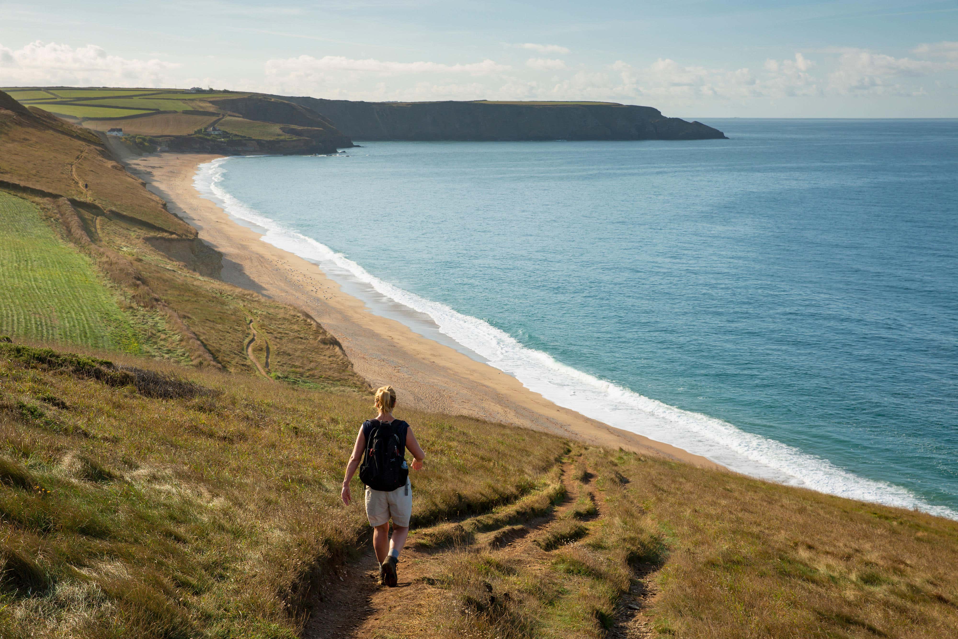 A woman strolls along the South West Coast Path above Porthleven Sands in Cornwall, England (Alamy/PA)
