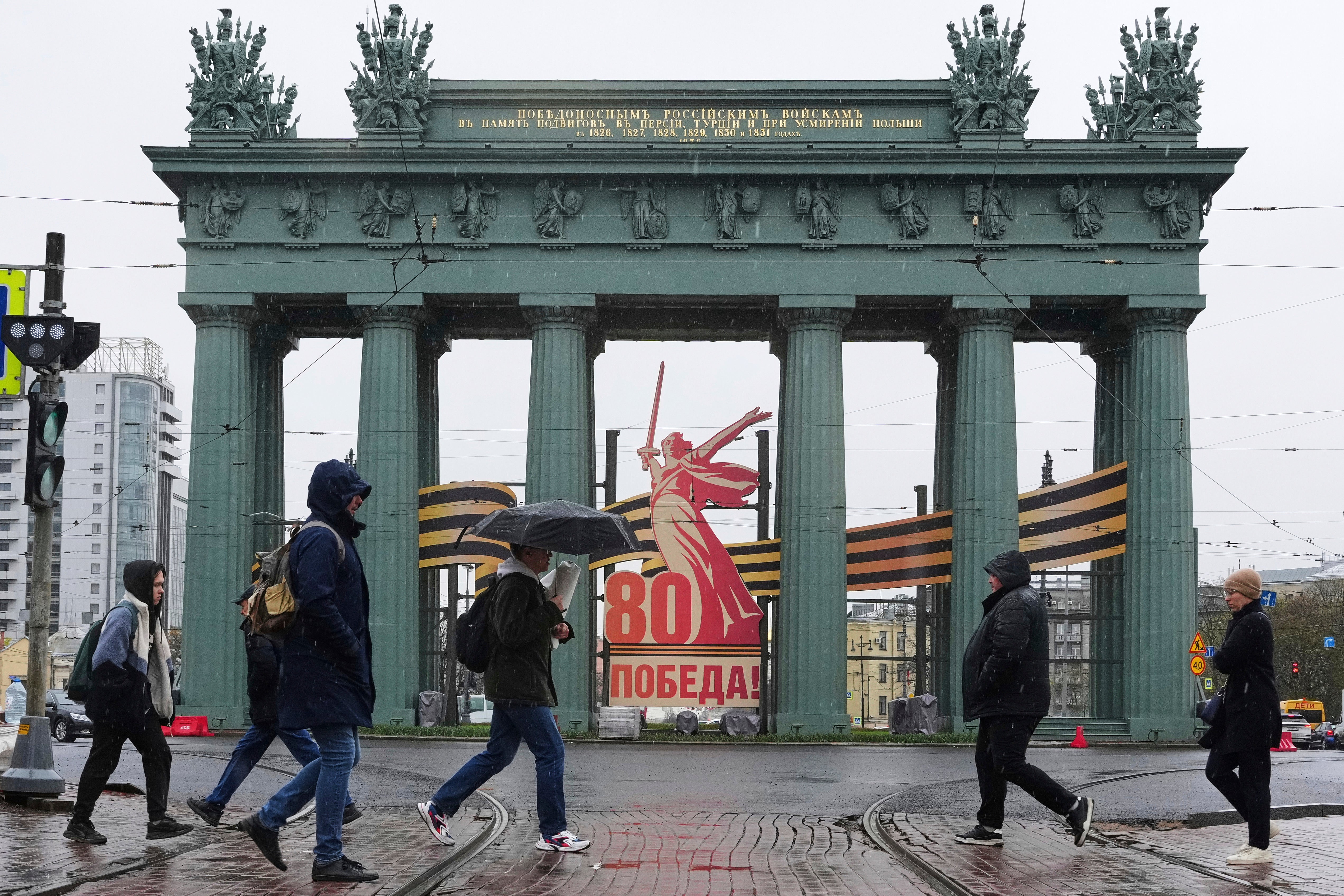 People cross a street in St. Petersburg, Russia, on Monday, April 28, 2025, in front of what is known as the Moscow Triumphal Gate