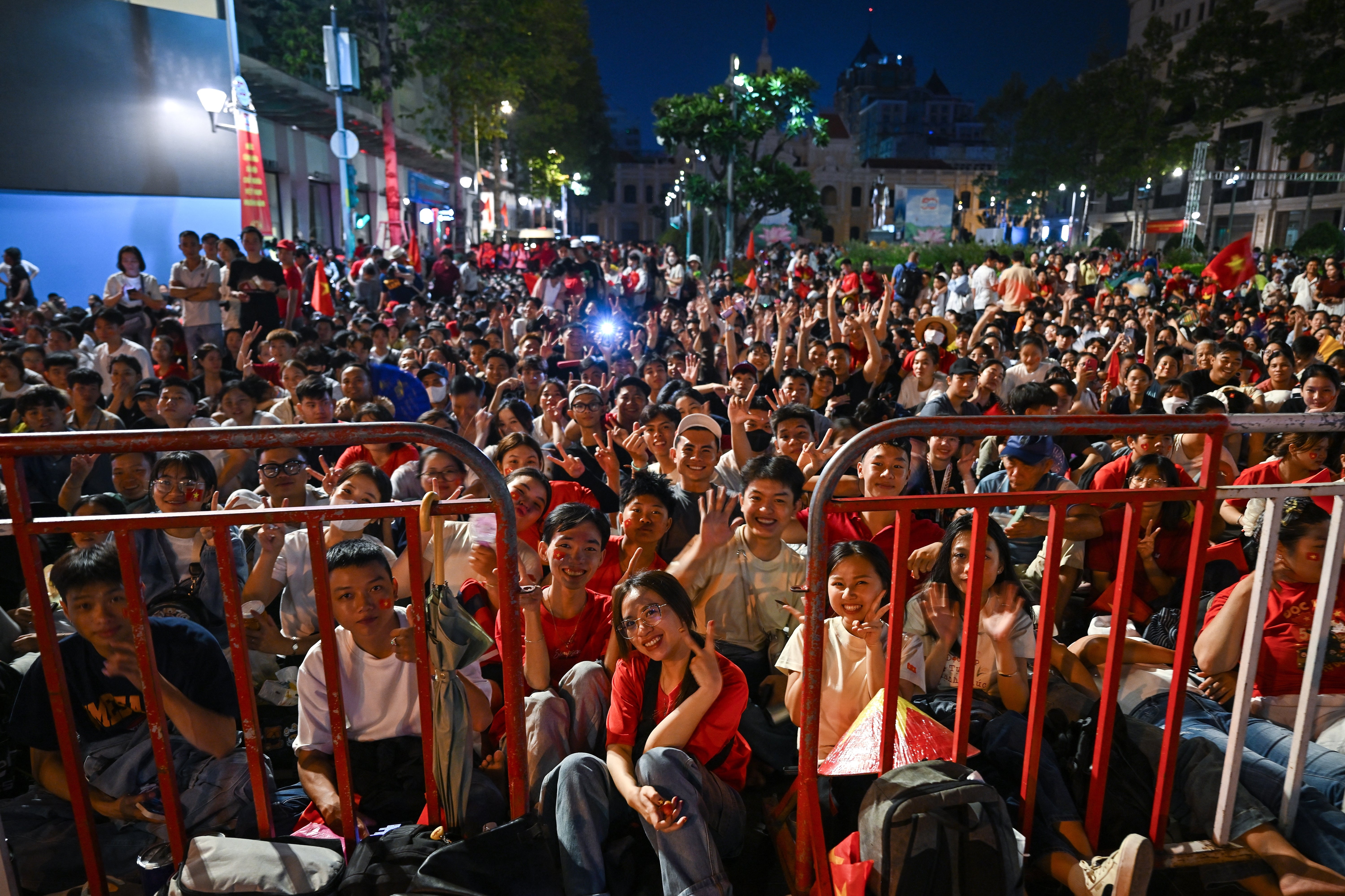 Spectators waiting overnight sit along a road to reserve their spot in Ho Chi Minh City