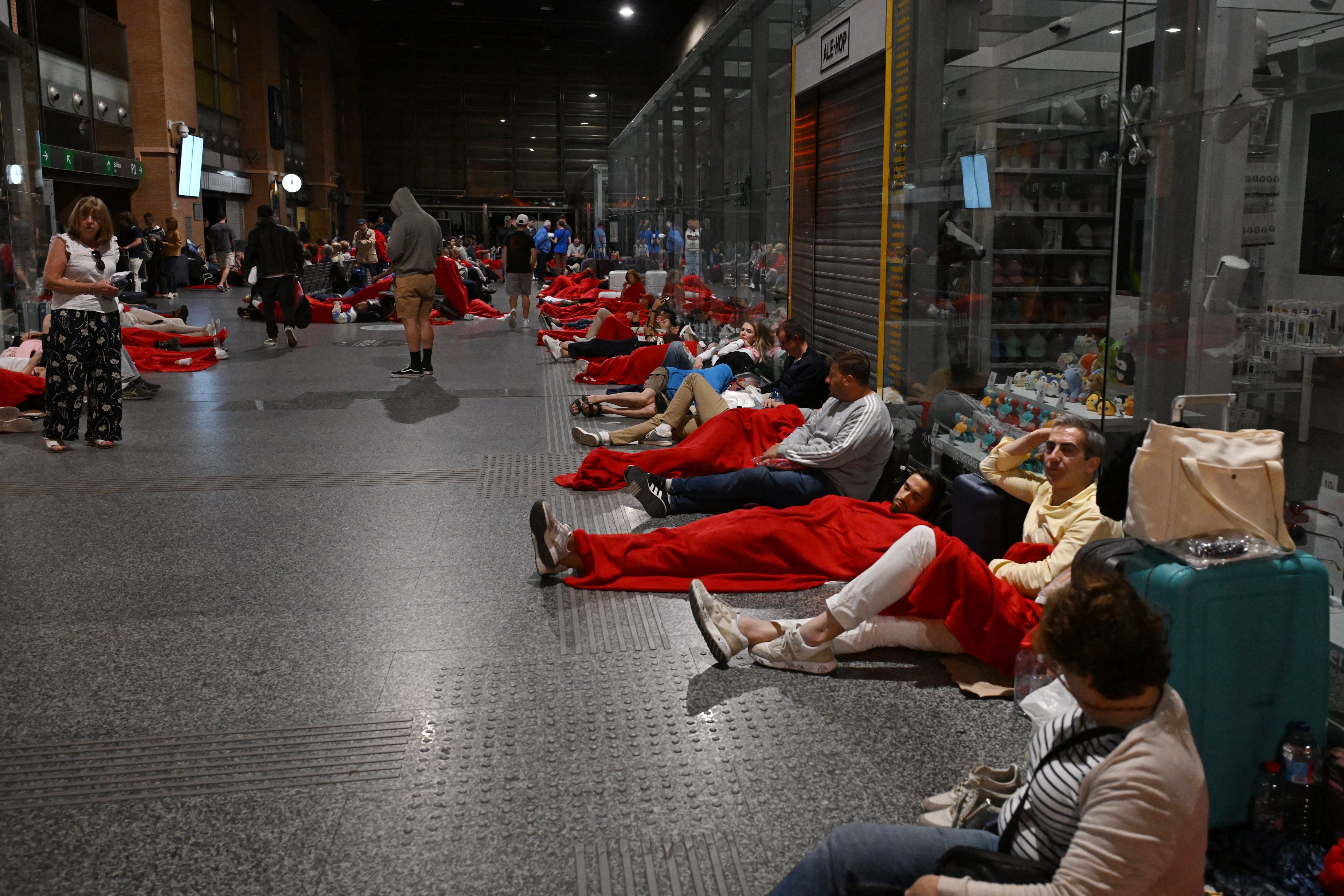 Travelers covered with Red Cross blankets lie on the floor, as they prepare to spend the night at the Cordoba train station, following a massive power cut affecting the entire Iberian peninsula and the south of France, on April 28, 2025