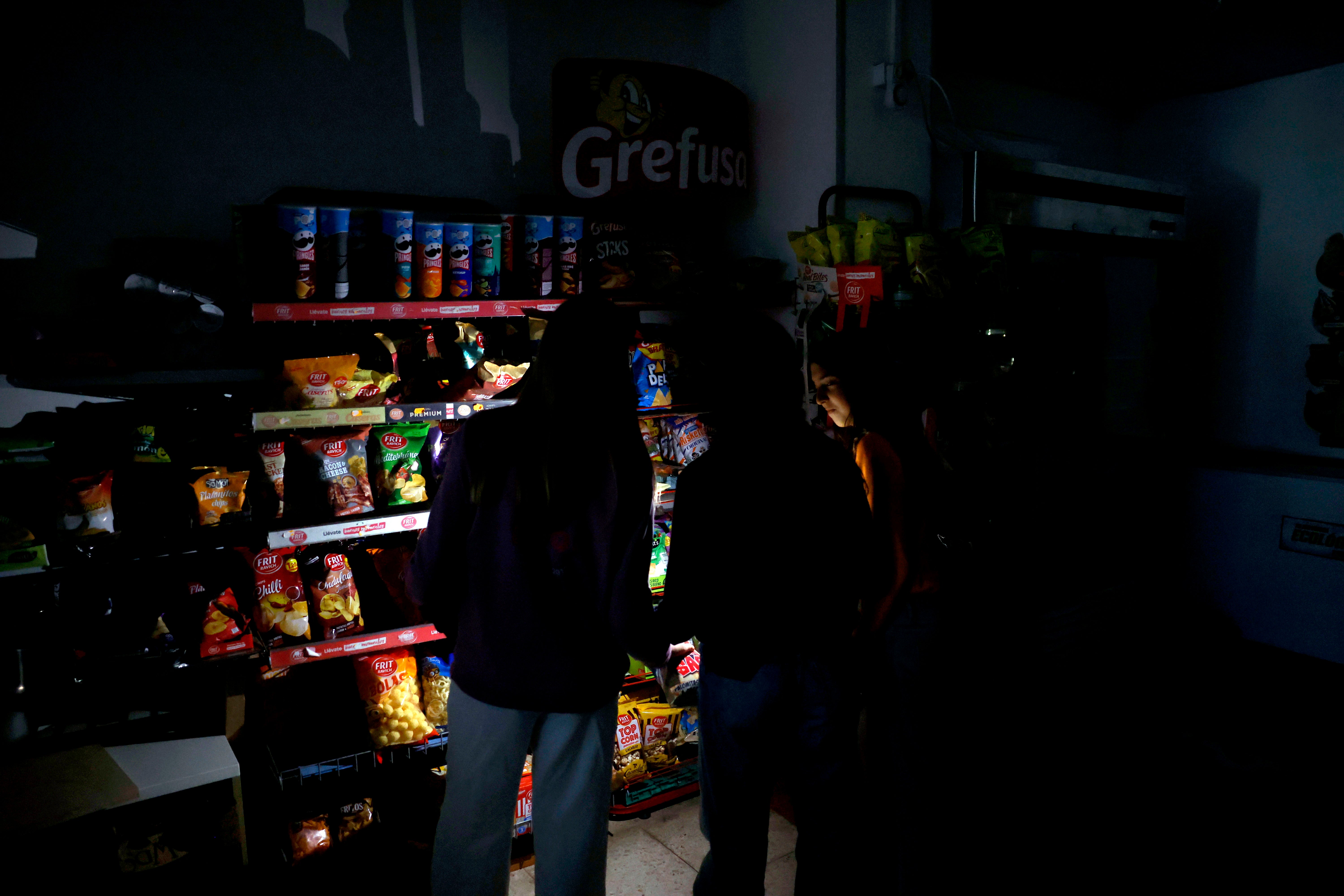 Customers use their mobile phone torches inside a supermarket during a power outage, in downtown Barcelona