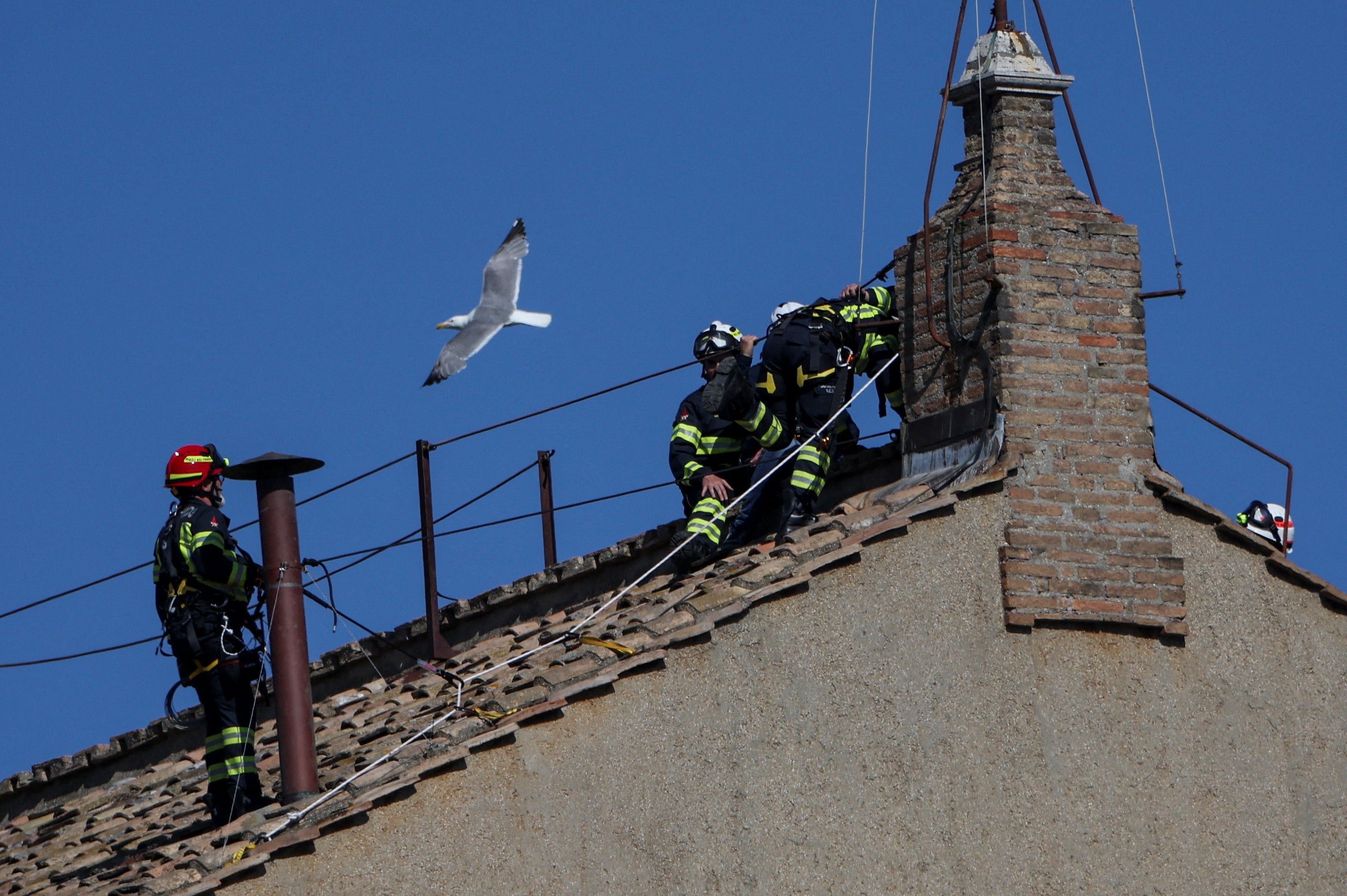A seagull flies near firefighters as they work on the roof of the Sistine Chapel to set a chimney, ahead of the conclave, at the Vatican May 2, 2025. REUTERS/Stoyan Nenov