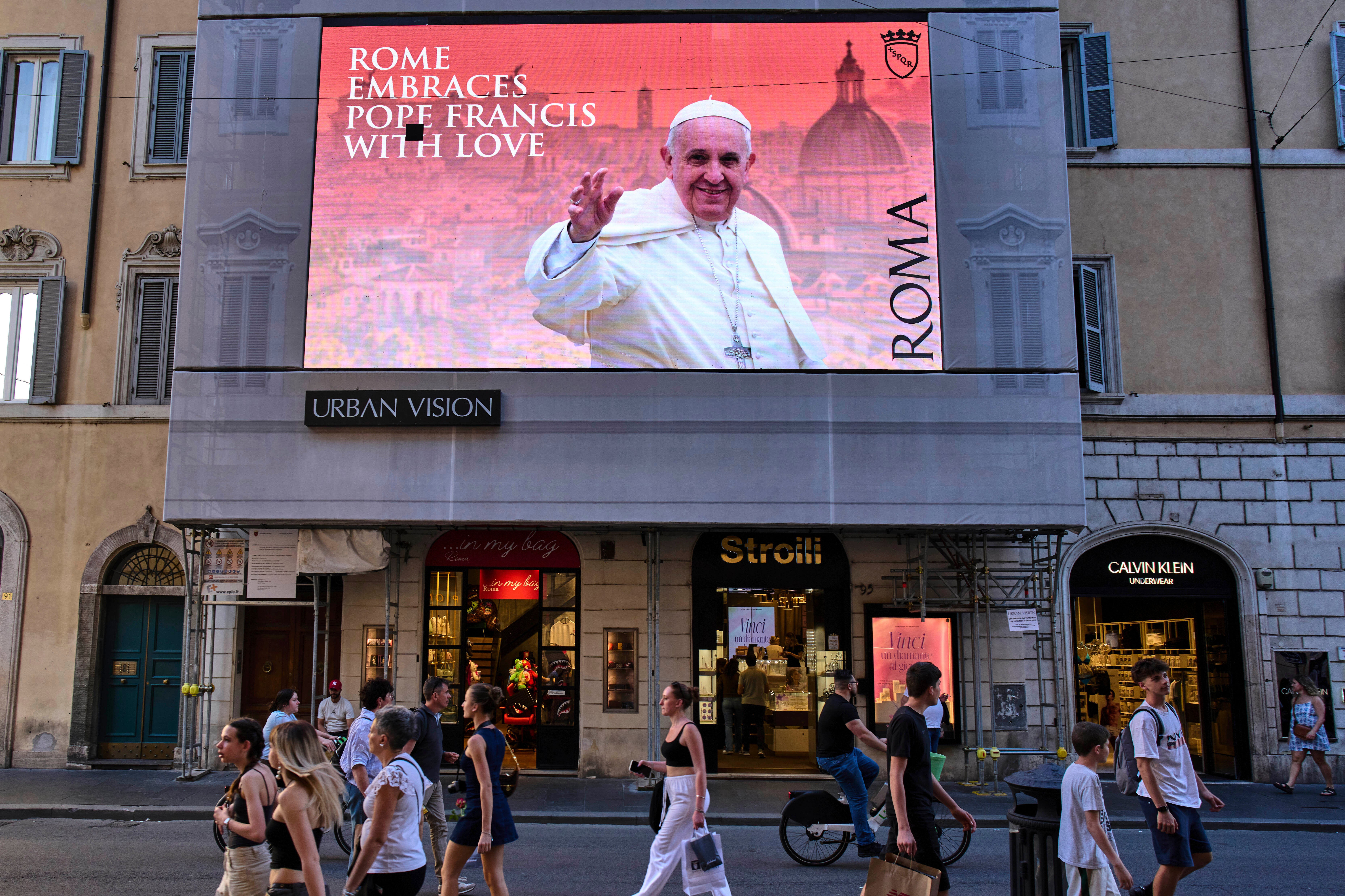 A street screen dedicated to Pope Francis reads "Rome hugs Francis with Love" in downtown Rome