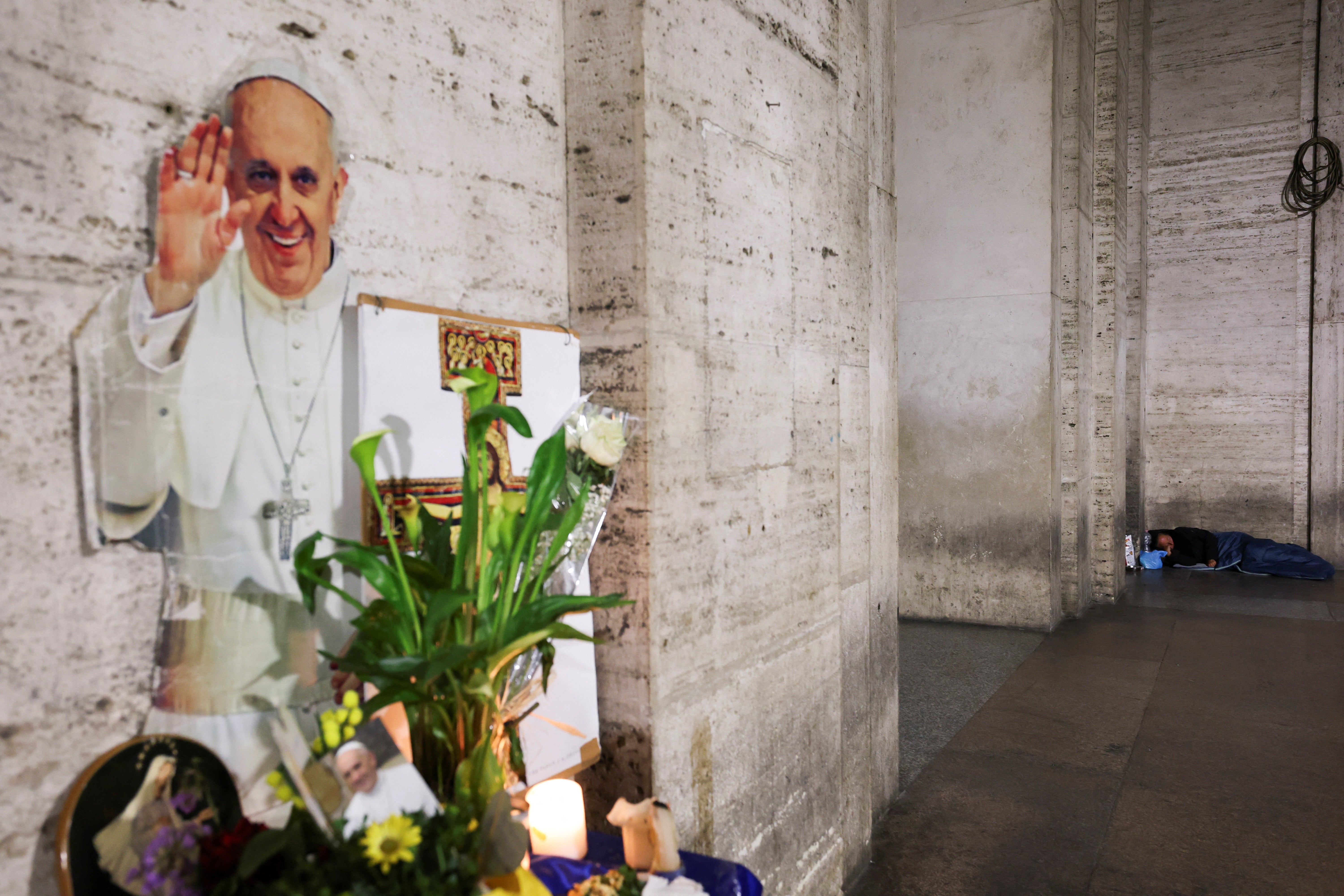 A homeless person sleeps near to a makeshift memorial for Pope Francis near St Peter's Square, as seen from Rome, Italy April 24, 2025. REUTERS/Kai Pfaffenbach