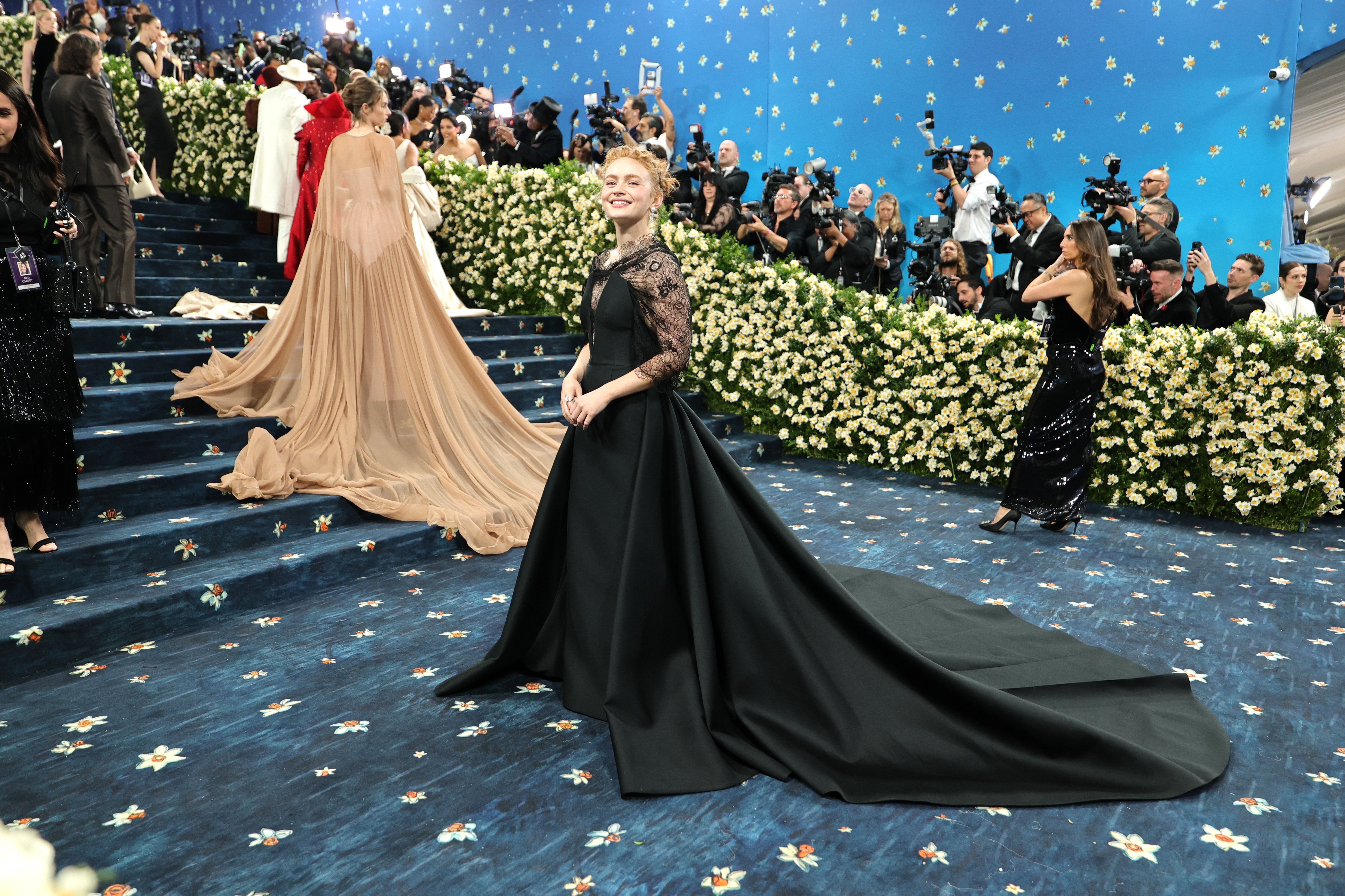 Sadie Sink showed up for the 2025 Met Gala in a simple black gown with a billowing train, lace sleeves, and dangly pearl earrings