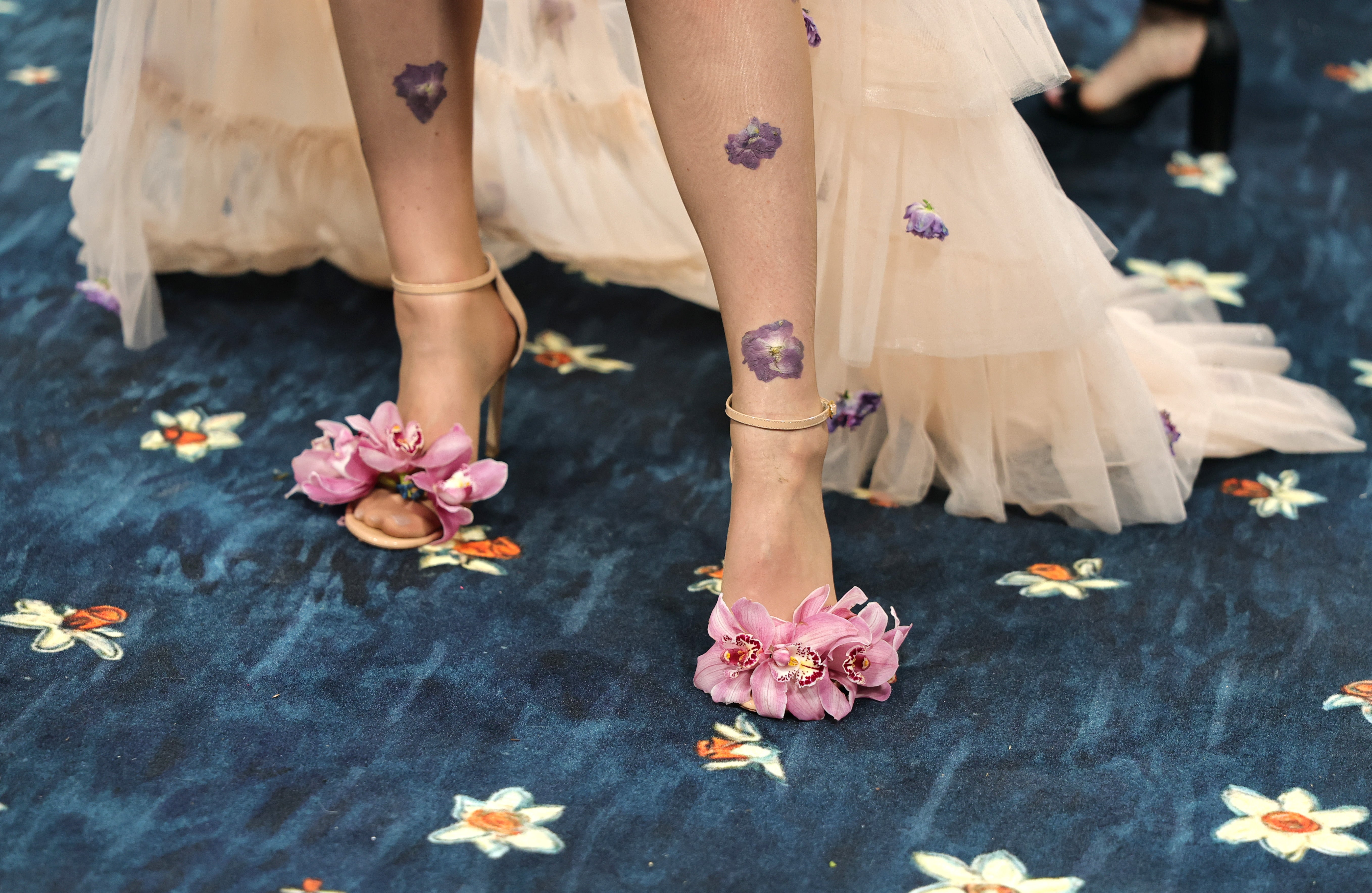 The artist’s outfit was adorned with strappy, open-toe heels with bright pink flowers pasted on top of the toes. Tiny purple flowers floated over her legs and around her pale pink skirt