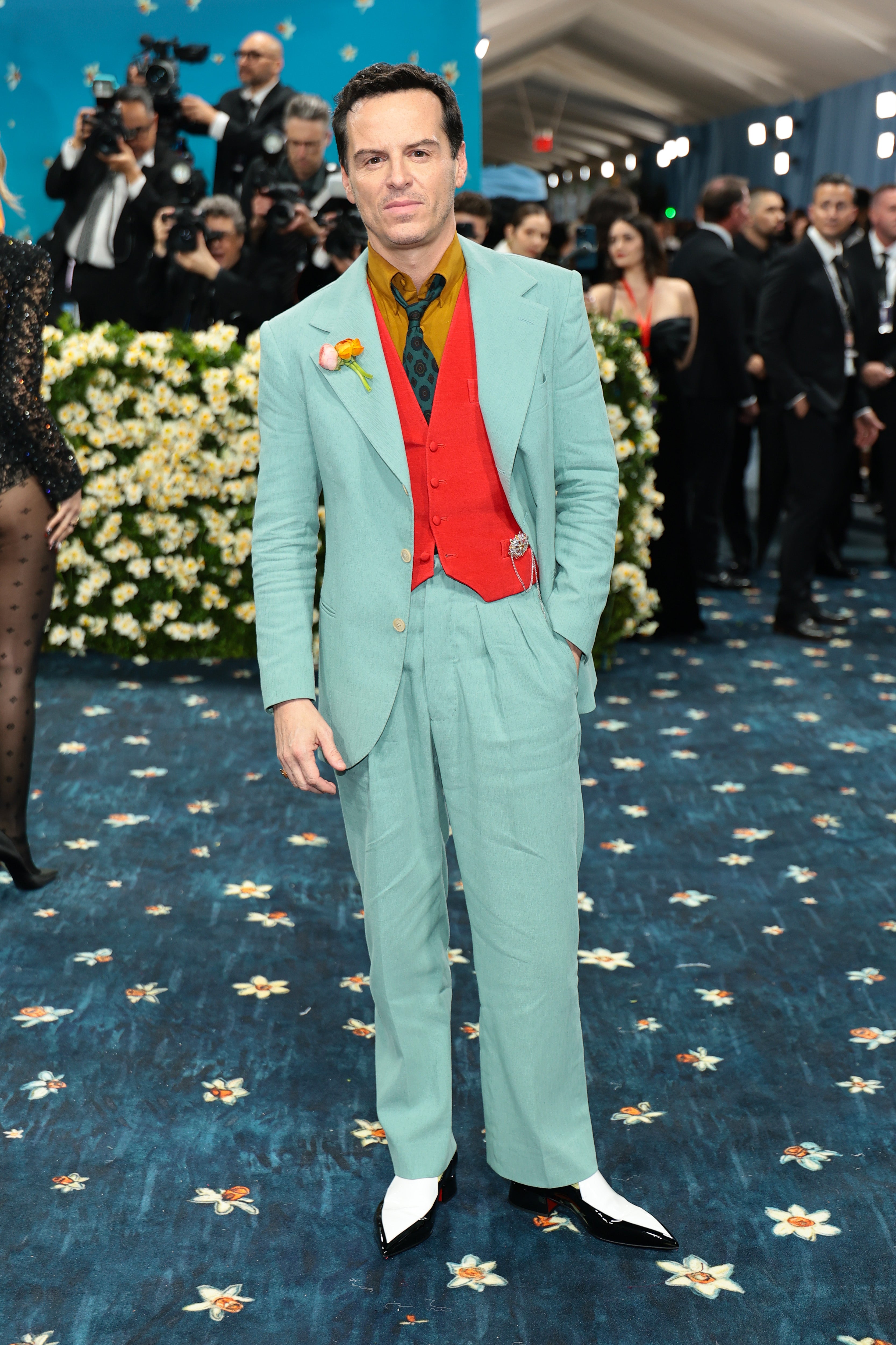Andrew Scott attended the 2025 Met Gala in a teal blue suit with a red vest, a mustard-colored shirt, and pointed-toe white shoes. The suit looked to be fashioned from a thin, wrinkly material and made him look a bit disheveled
