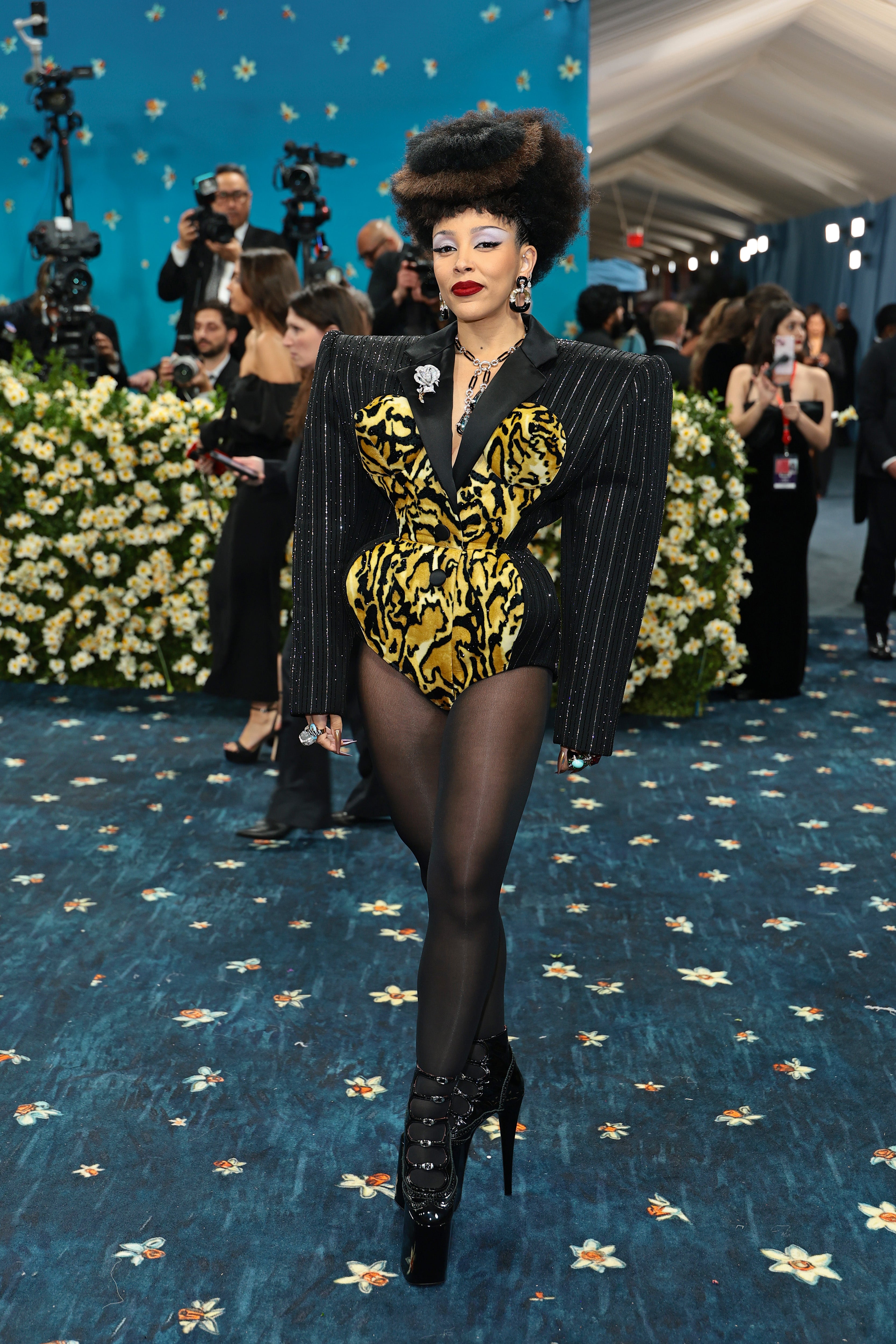Doja Cat wore a custom pinstripe bodysuit with dramatic shoulder pads by Marc Jacobs. The long-sleeved outfit featured a cutout tiger print. She also wore sheer tights and black heels, as her hair was teased and styled in an updo