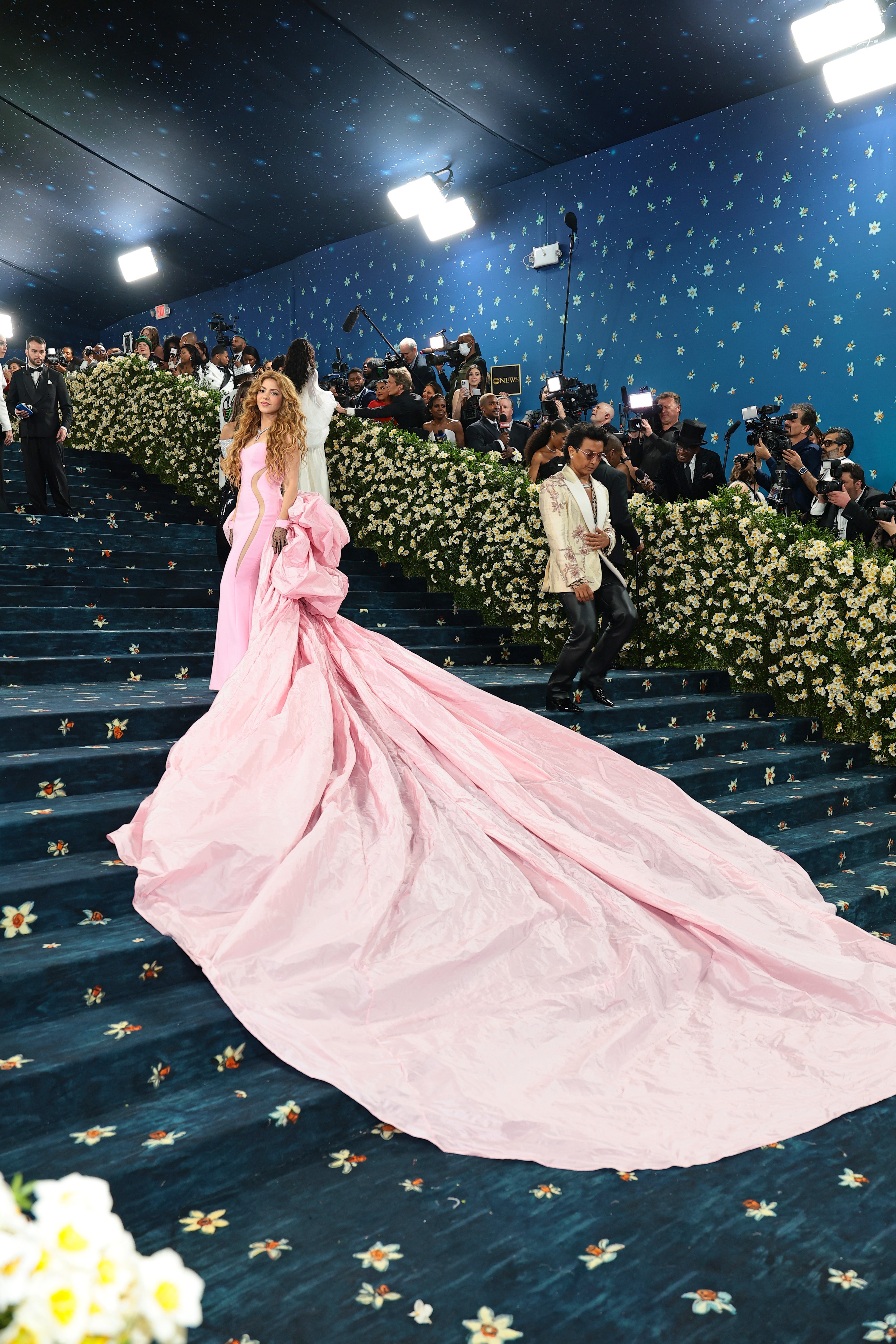Shakira stepped onto the navy blue carpet for the 2025 Met Gala on Monday in a bubblegum pink gown with an elongated train that nearly stretched all the way to the sides of the walkway