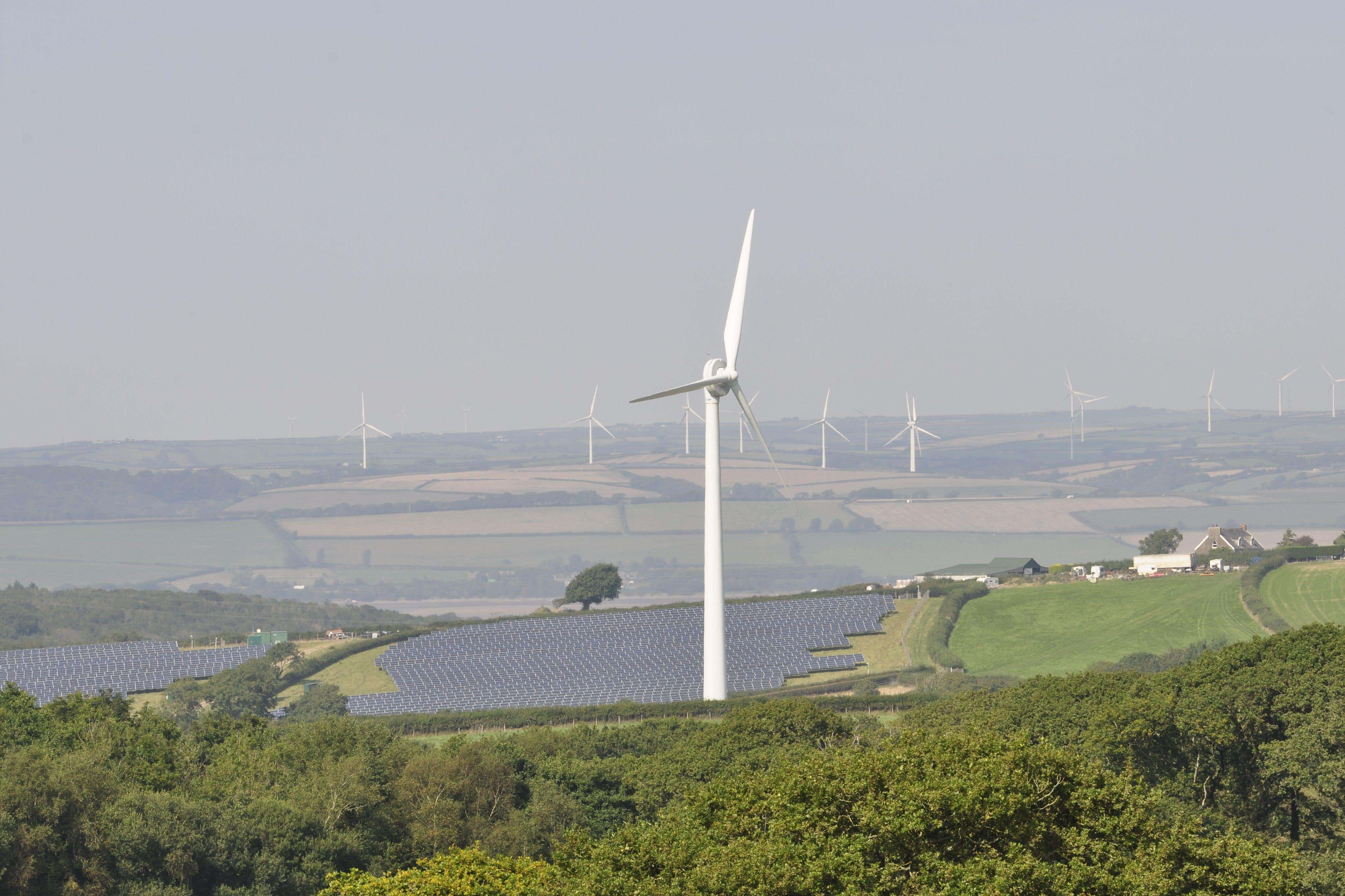 Wind turbines and solar panels on farmland in Devon (Alamy/PA)