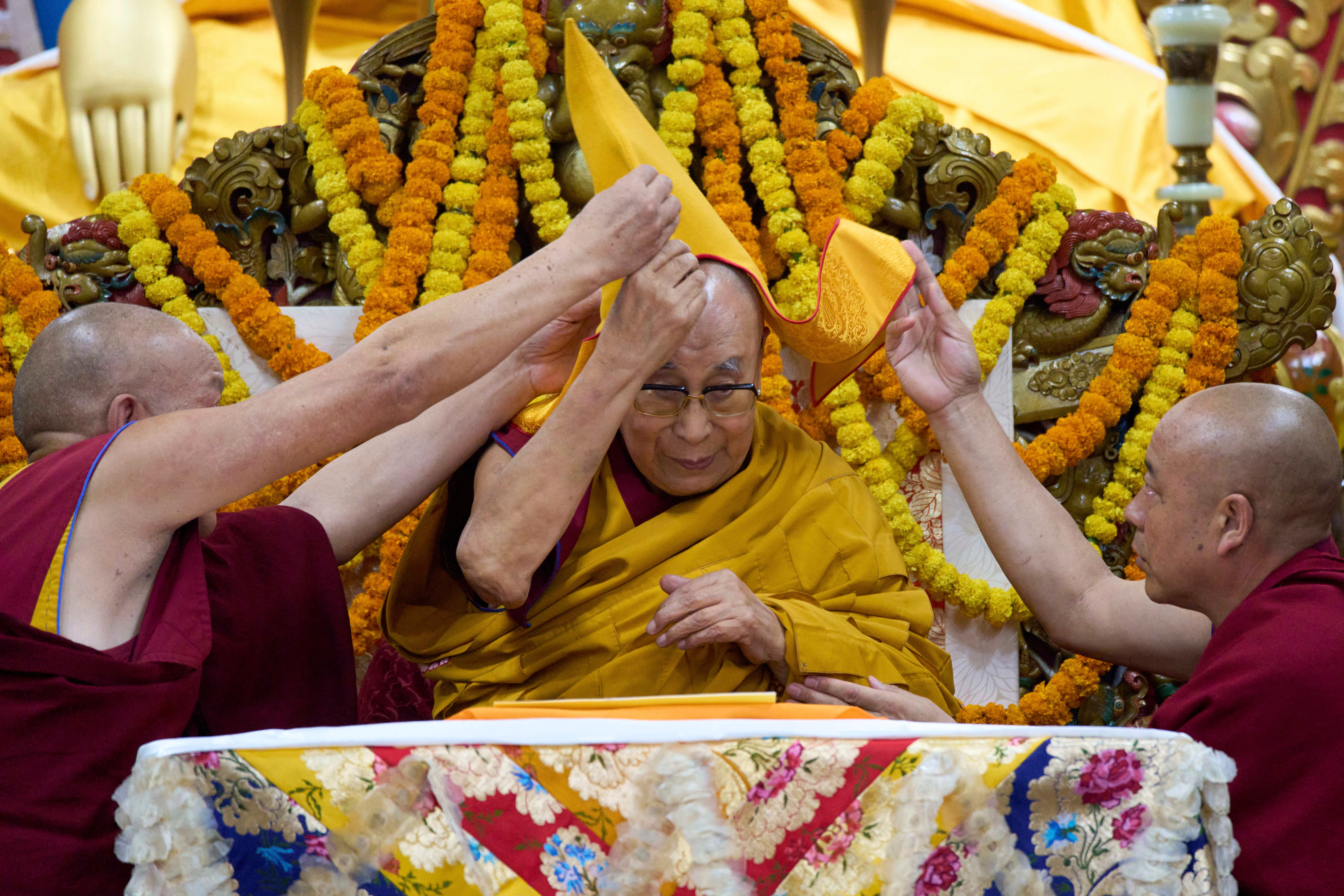 Attendant monks help the Dalai Lama wear a ceremonial hat at an event during which exiled Tibetans prayed for his longevity at the Tsuglakhang temple in Dharamshala, India, in May