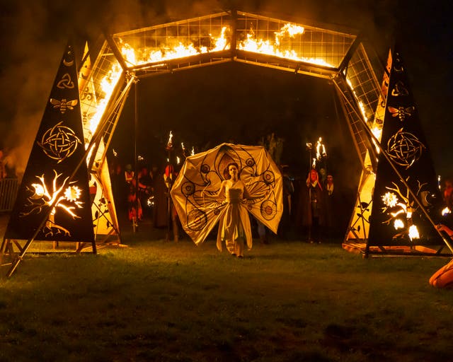 <p>This year's winged May Queen walks through a fire arch in The Dell</p>