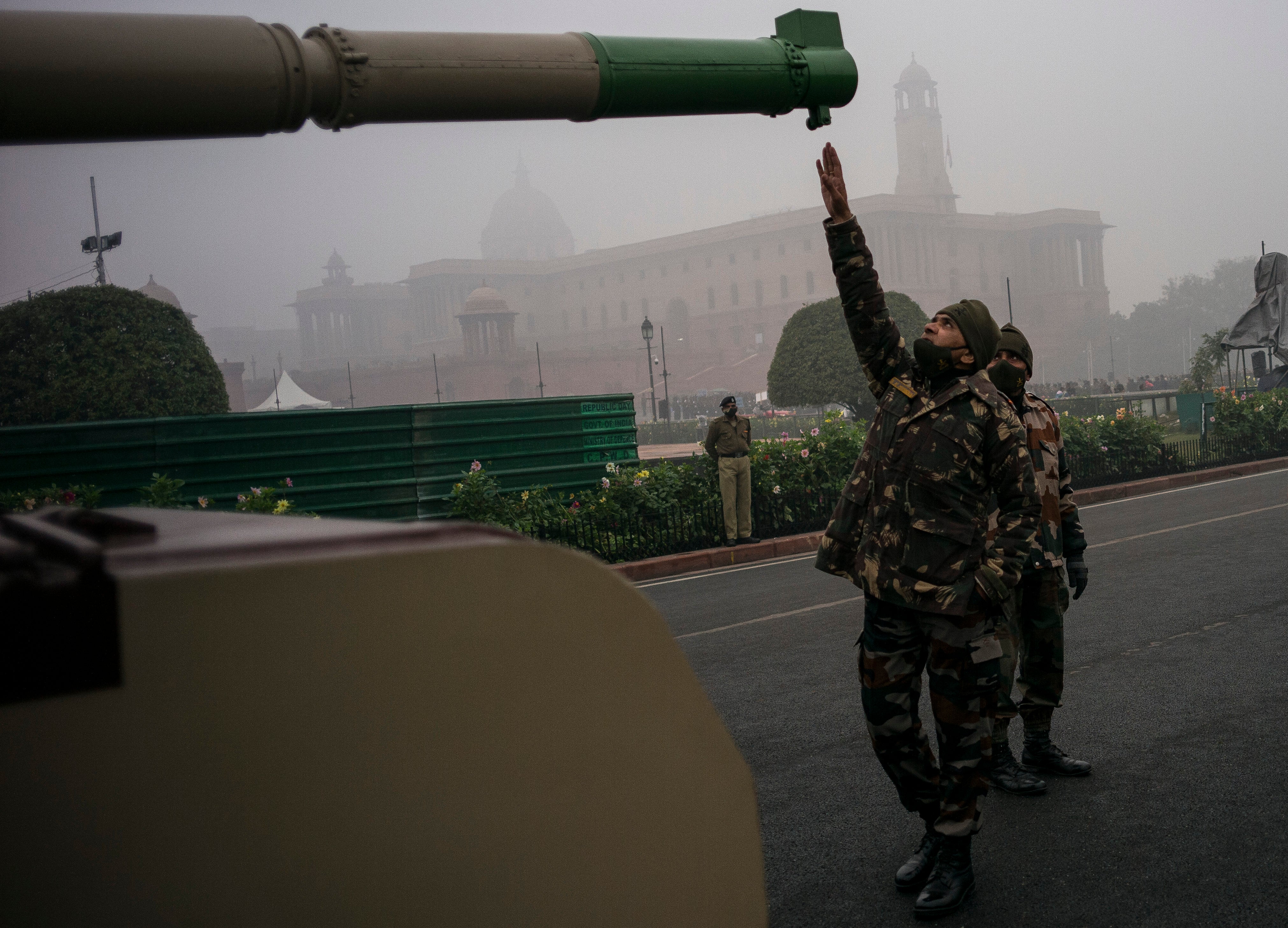 An Indian soldier raises his hands as he guides an operator sitting inside a tank ahead of rehearsals for parade