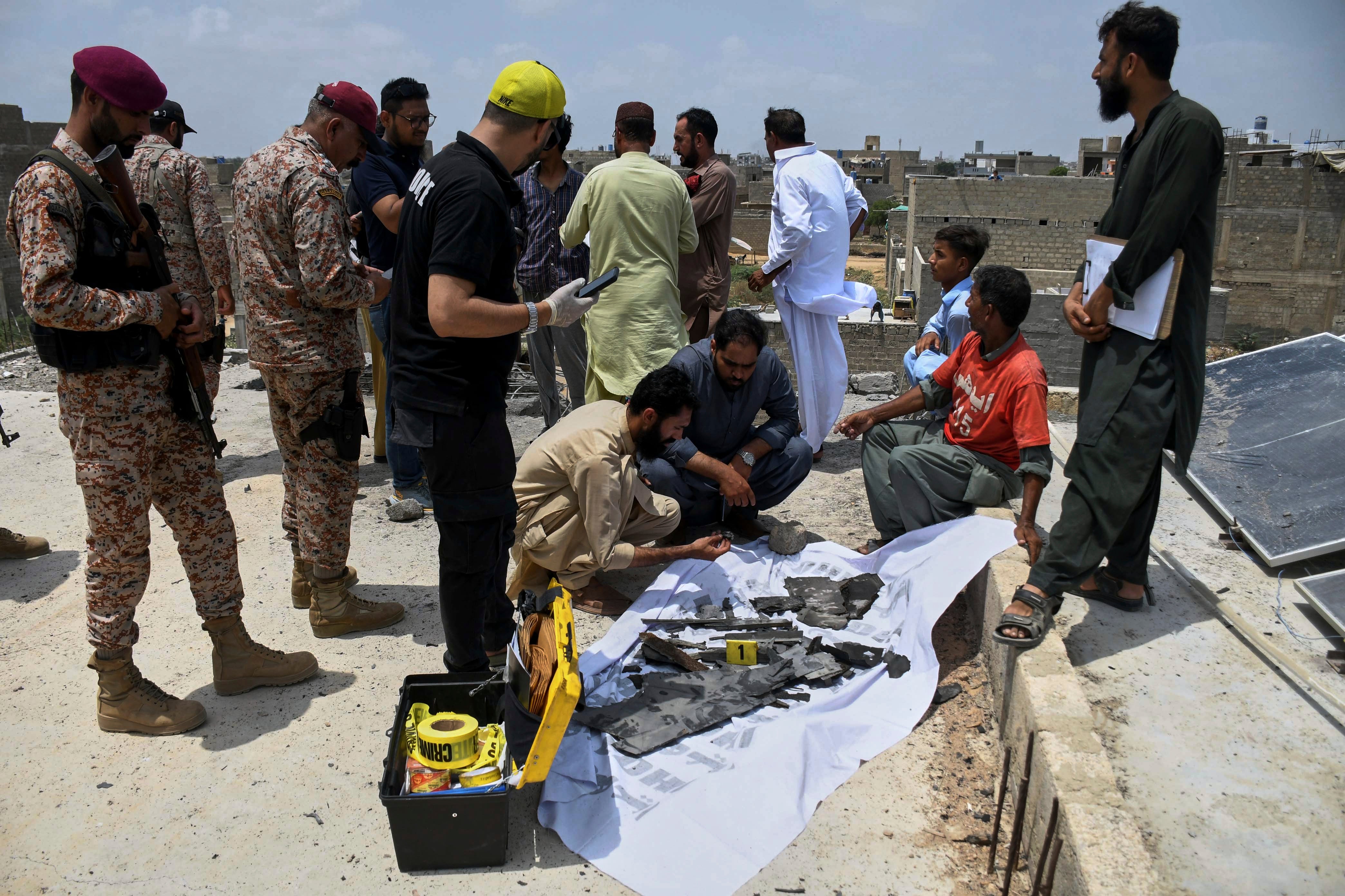 Paramilitary soldiers stand guard as investigators collect pieces of a suspected Indian drone at the site of a drone crash in Karachi, Pakistan