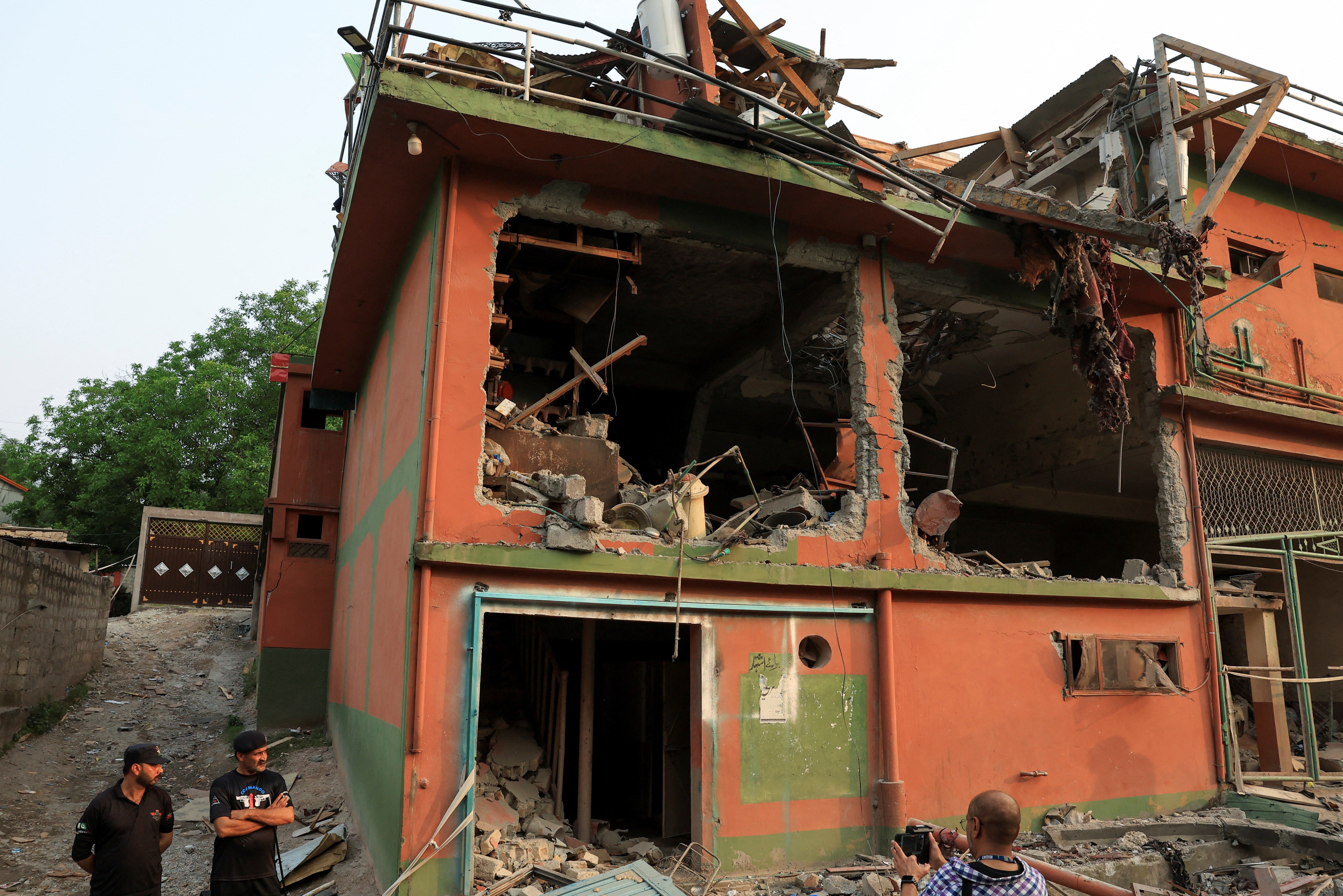 Police officers look on as a cameraman films the Bilal Mosque after it was hit by an Indian strike in Muzaffarabad