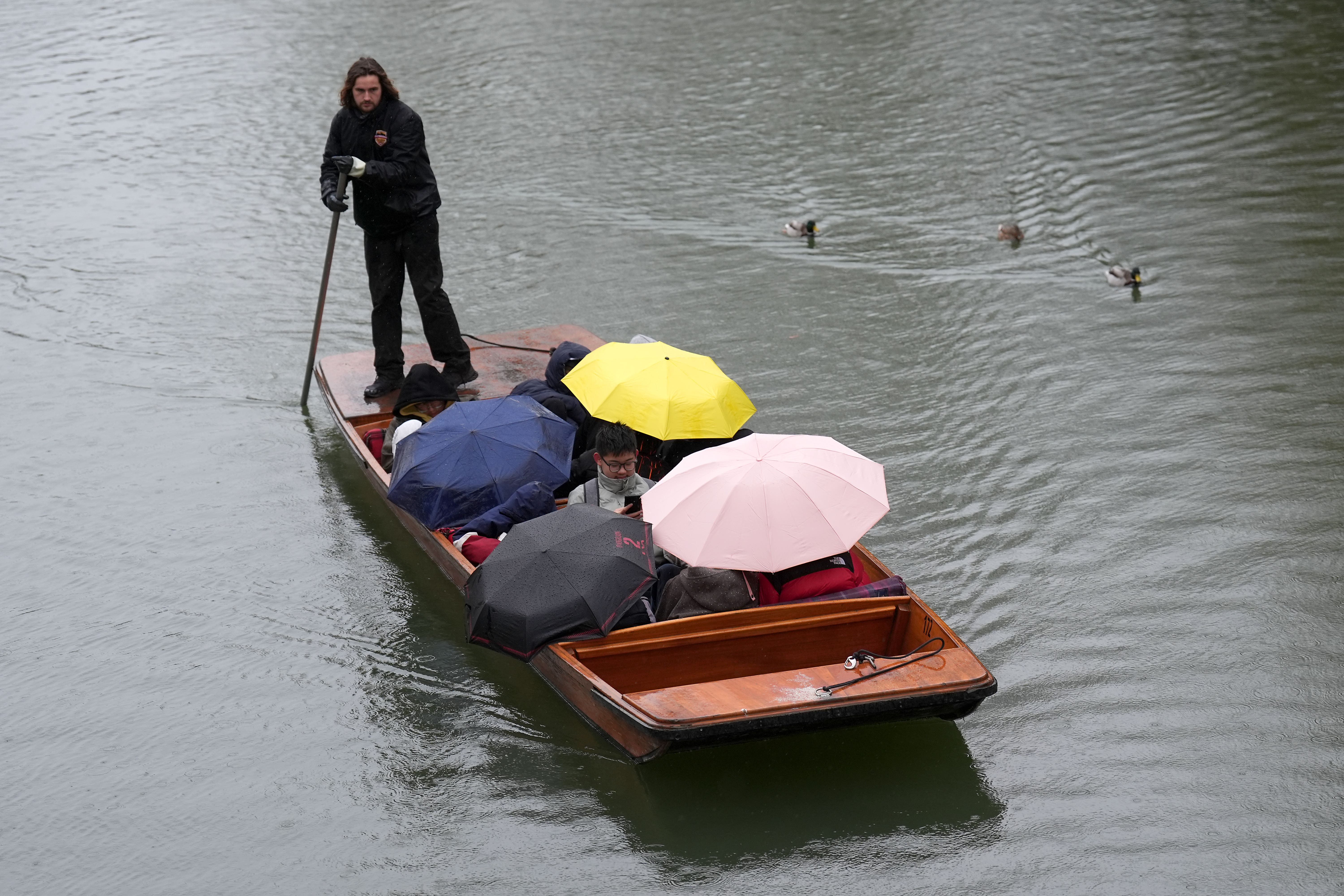 People shelter from the rain under umbrellas as they punt along the River Cam in Cambridge (Joe Giddens/PA)