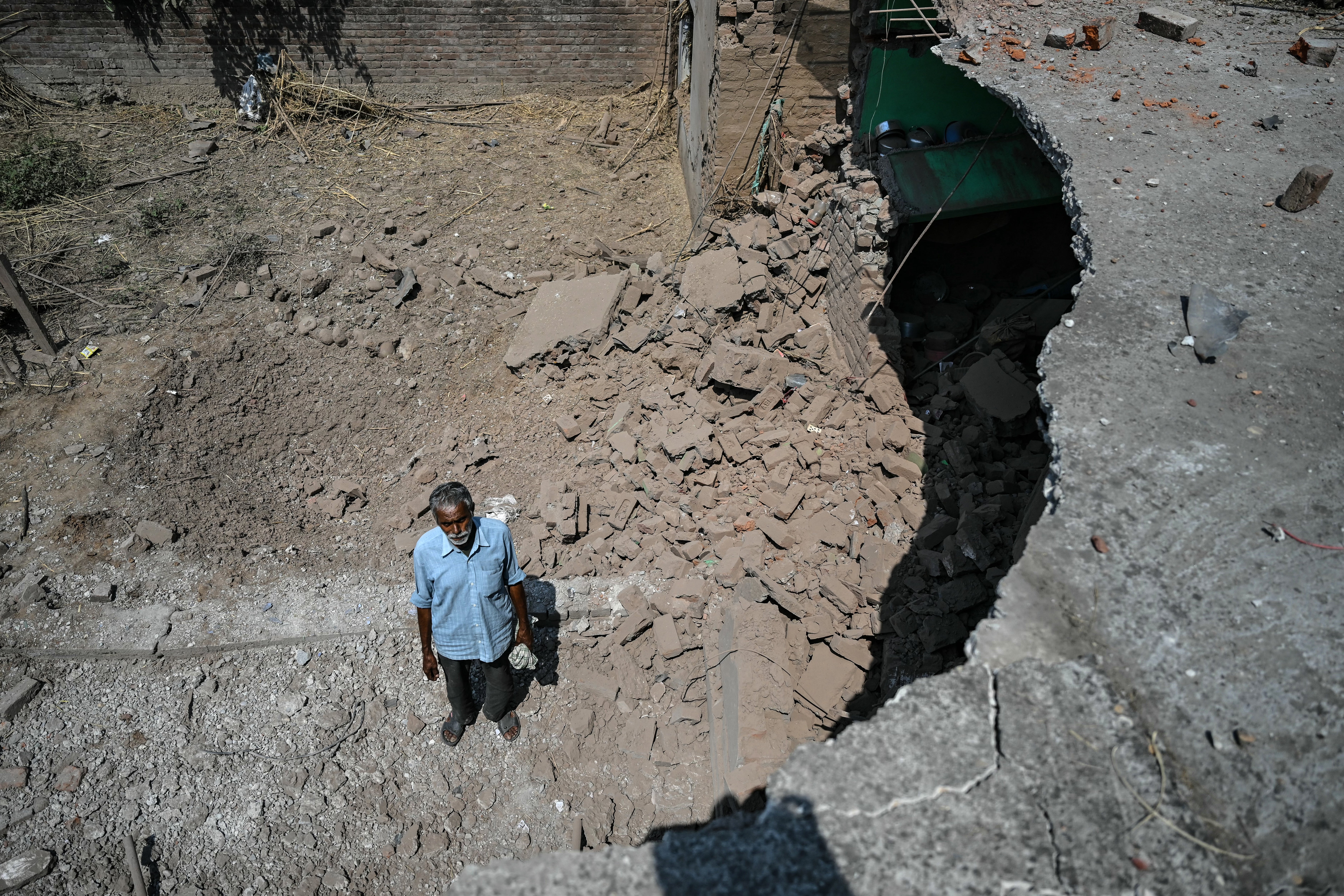 Bairi Ram, a local resident, stands beside the remains of his house after it was damaged by overnight Pakistani artillery shelling in Kotmaira village near the line of control in India’s Jammu region