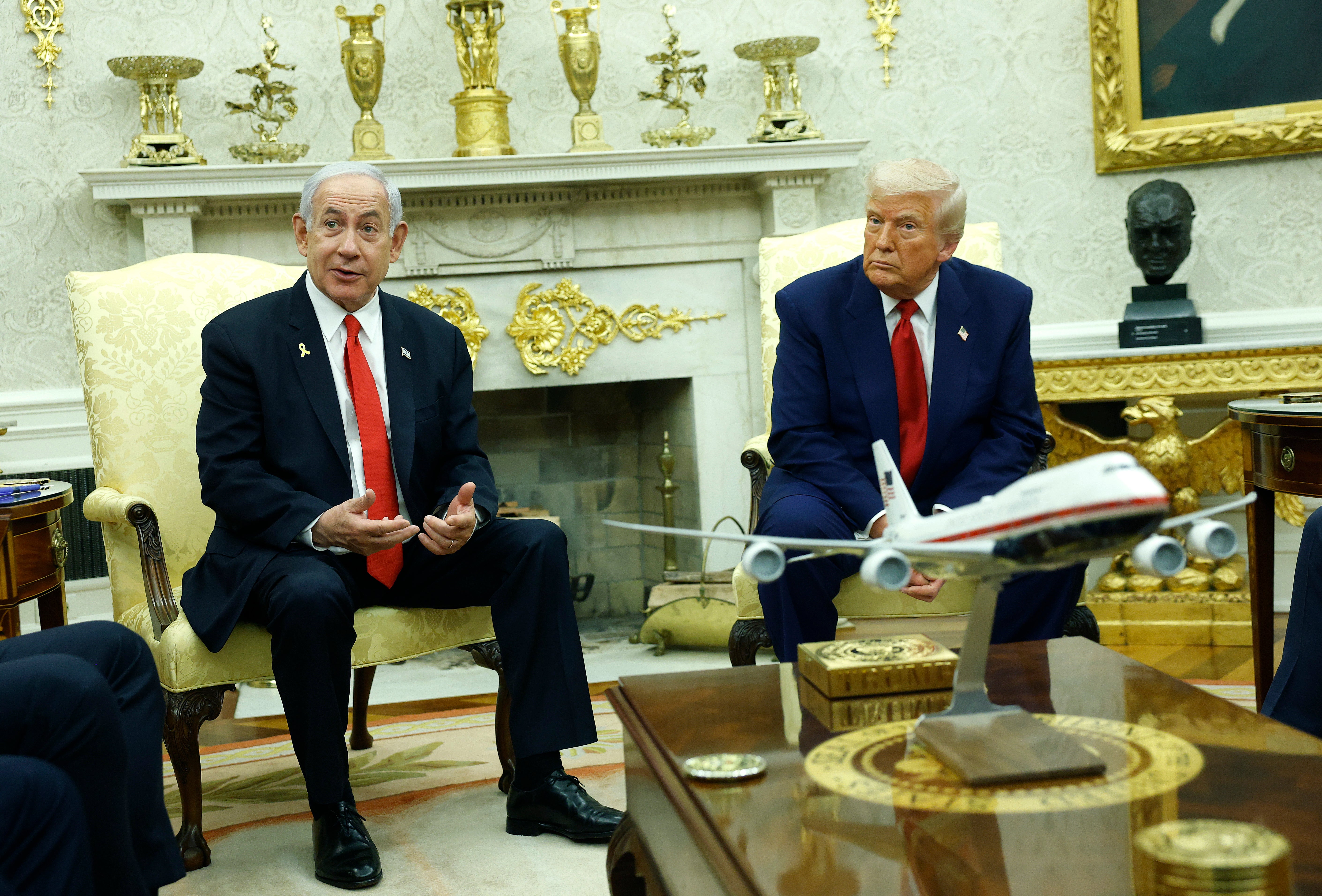 President Donald Trump sits in the Oval Office behind a model of the new version of Air Force One on order from Boeing that won't be delivered until 2027 at the earliest