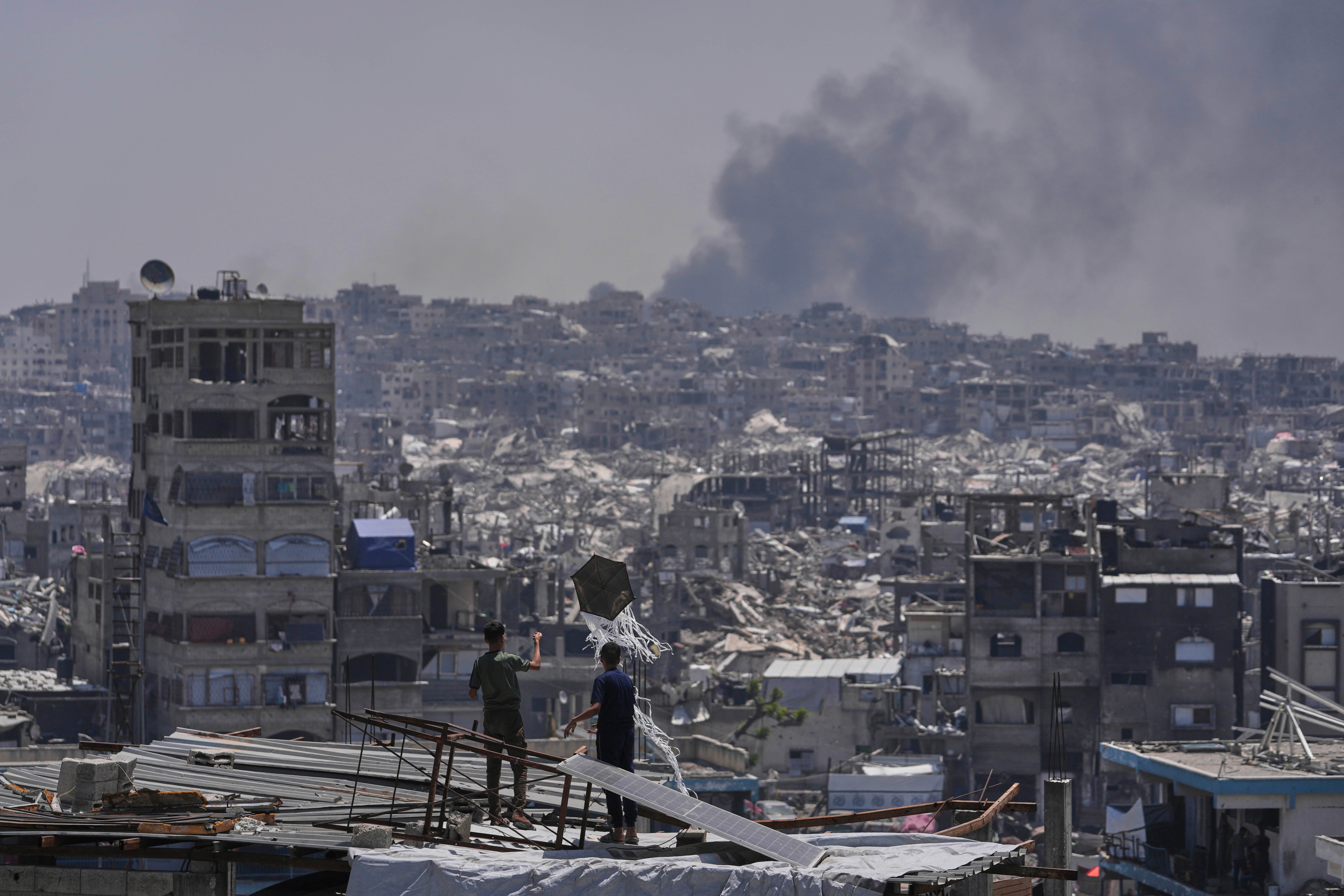Palestinians look on as smoke rises following an Israeli airstrike near Jabalia, northern Gaza Strip