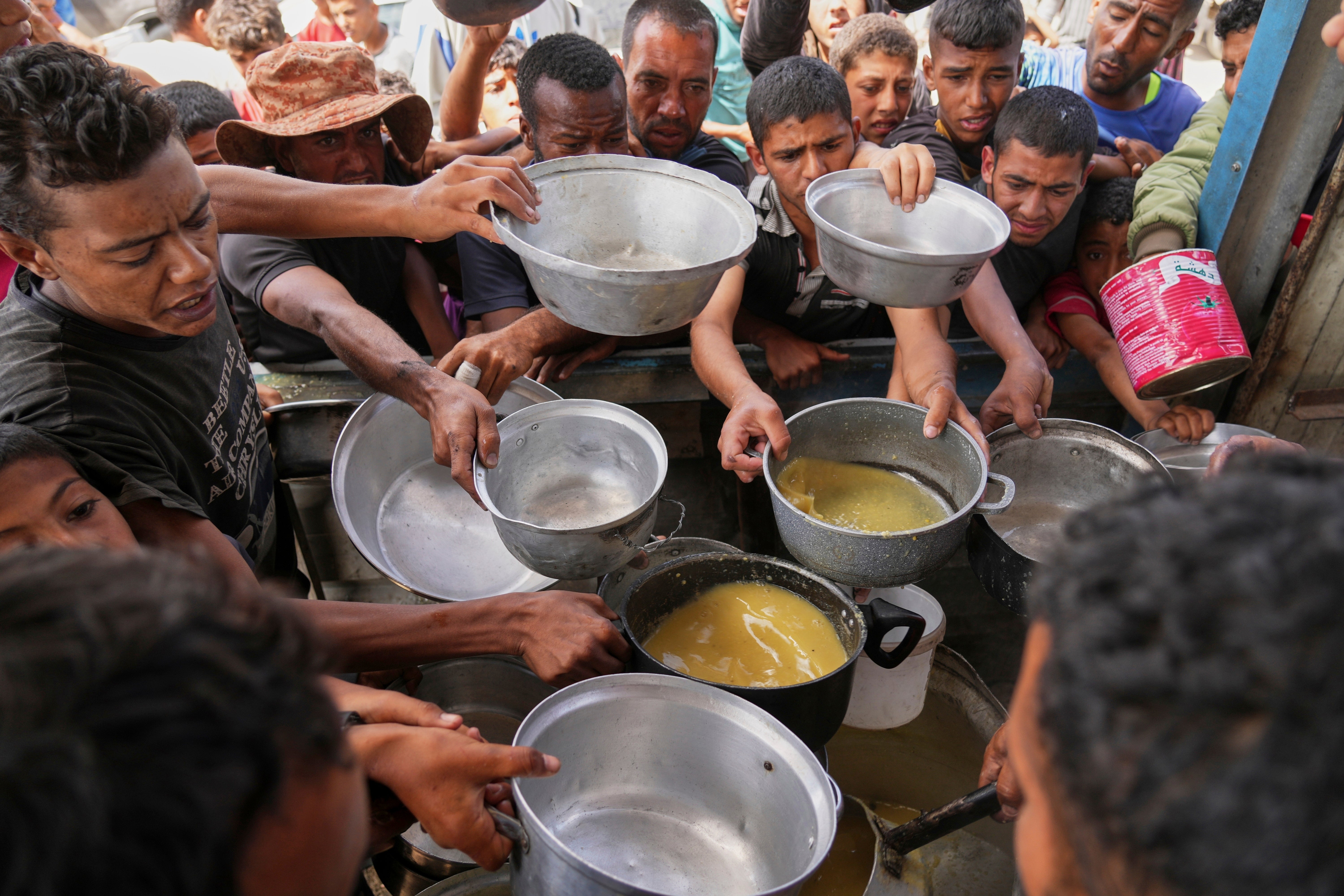 Palestinians struggle to receive cooked food distributed at a community kitchen in Khan Younis