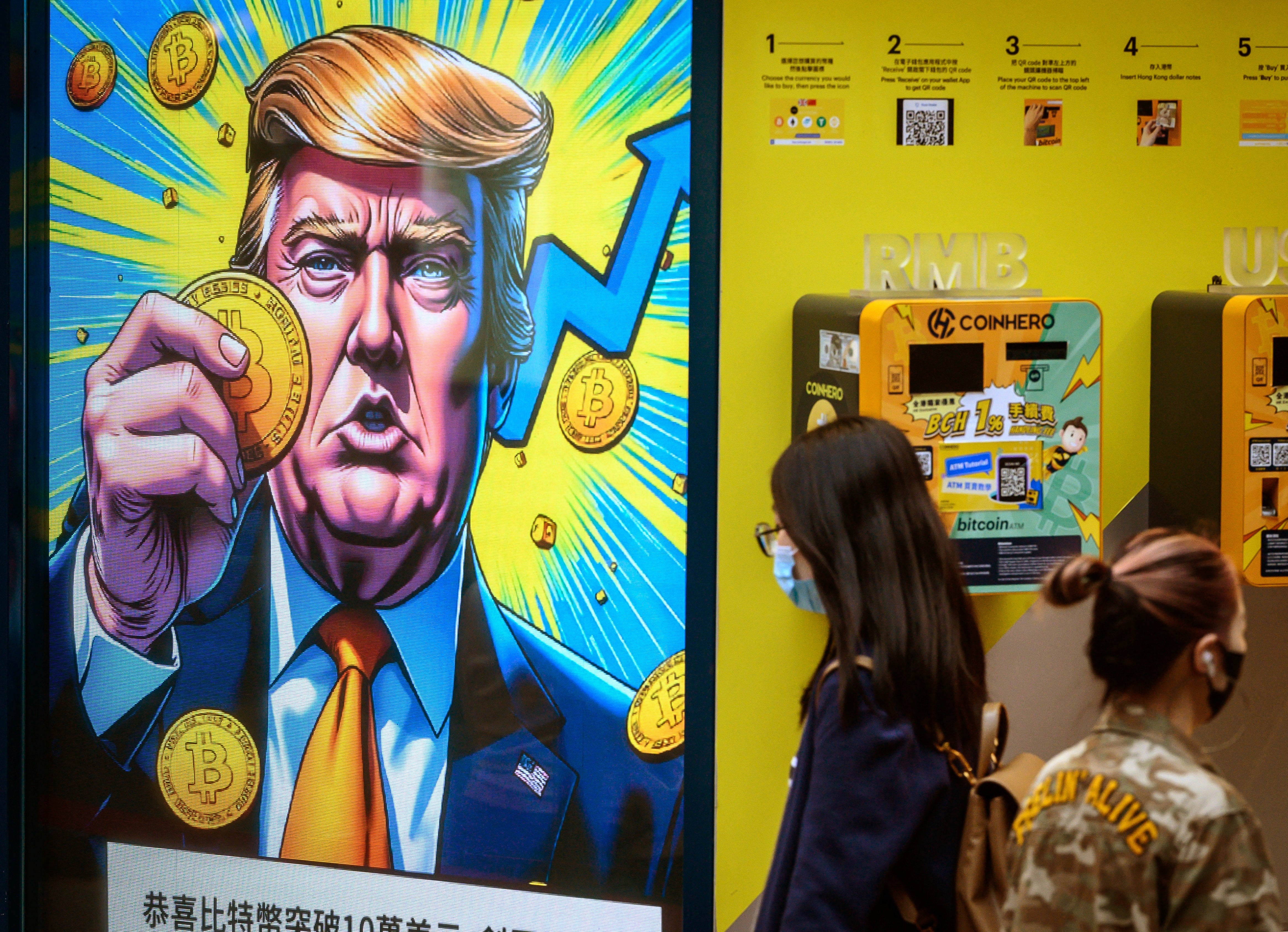 People walk past a cryptocurrency exchange office with a screen featuring US President Donald Trump holding cryptocurrency