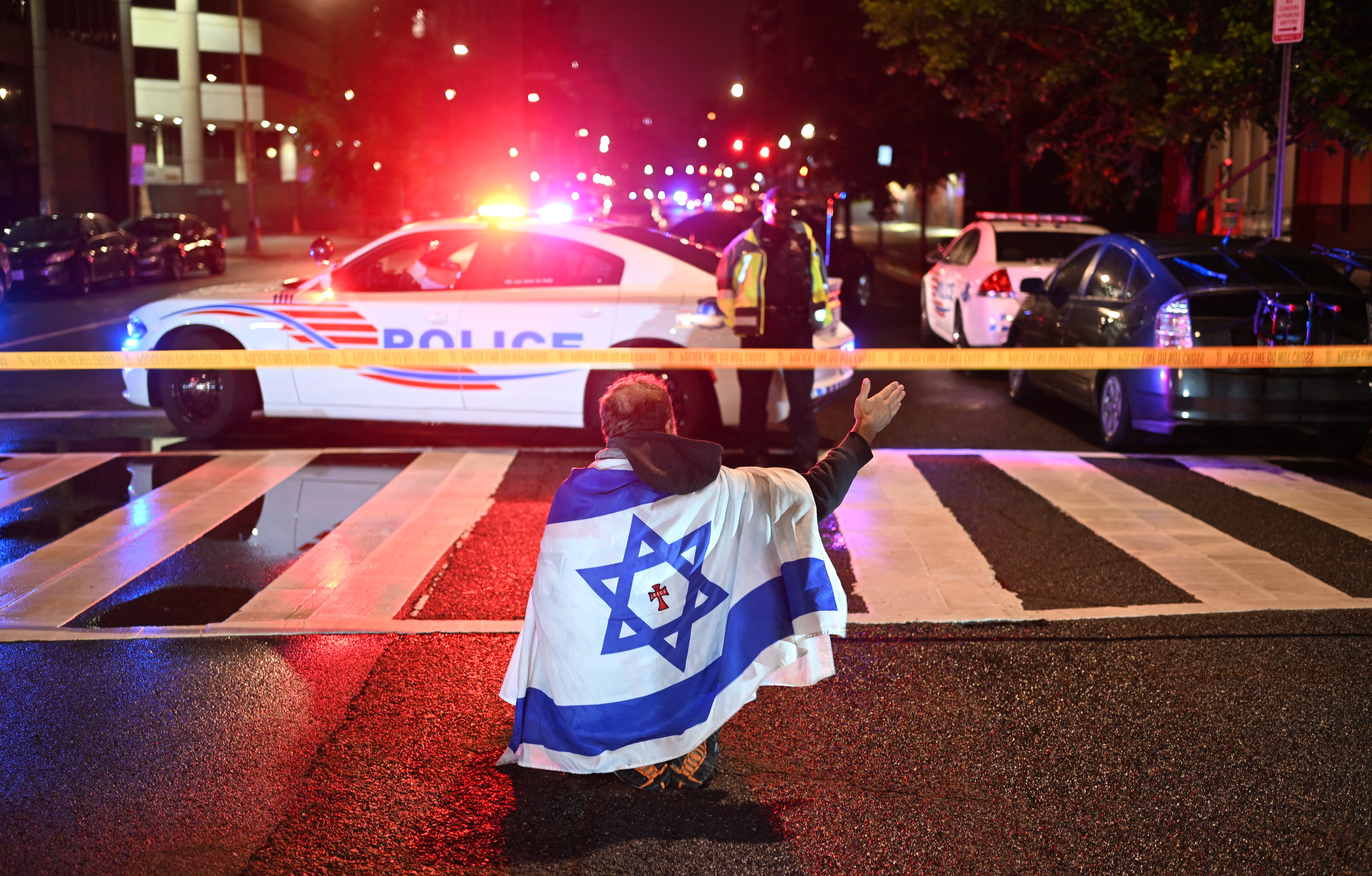 A man draped in the Israeli flag as as Metropolitan Police officers secure the area outside the Capital Jewish Museum