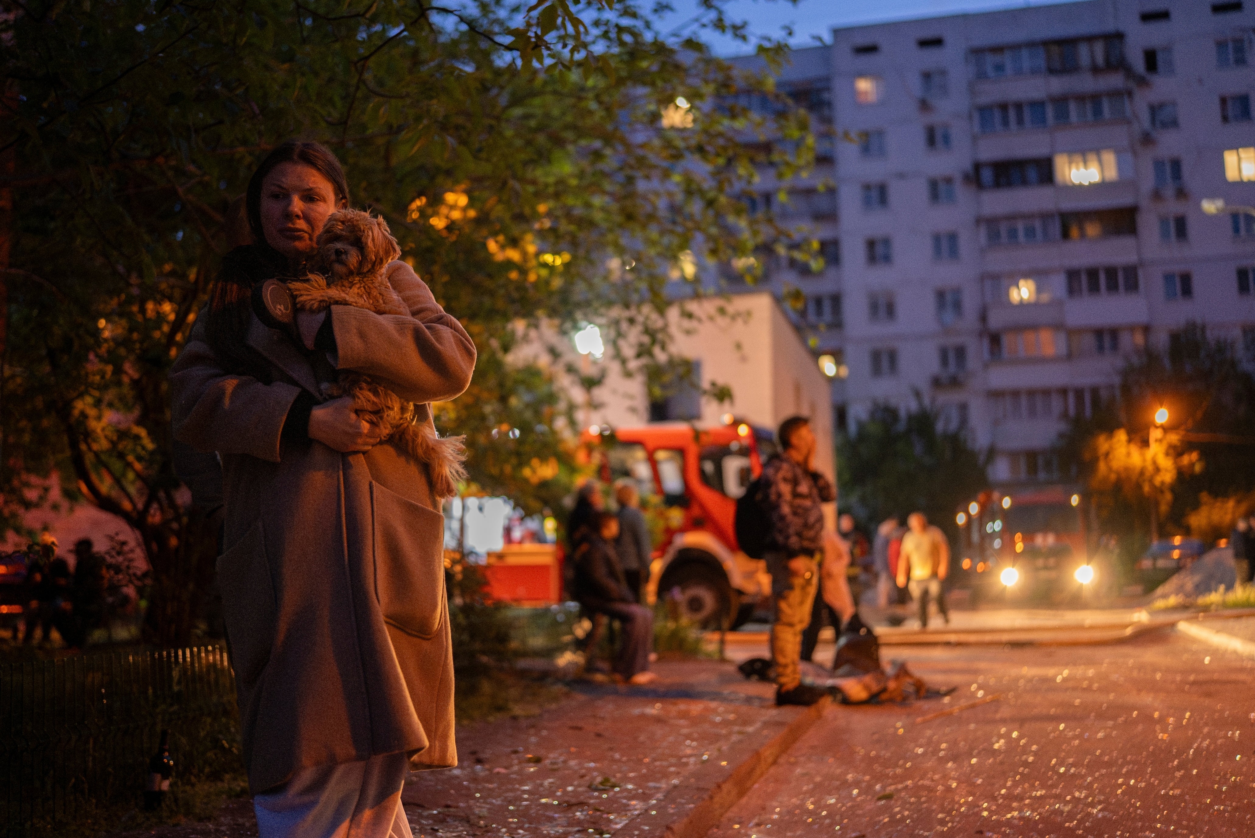 A woman carries her dog as she walks on a street with pieces of broken glass at the site of a residential building that was damaged after a Russian attack in Kyiv, Ukraine, Saturday, May 24, 2025. (AP Photo/Alex Babenko)