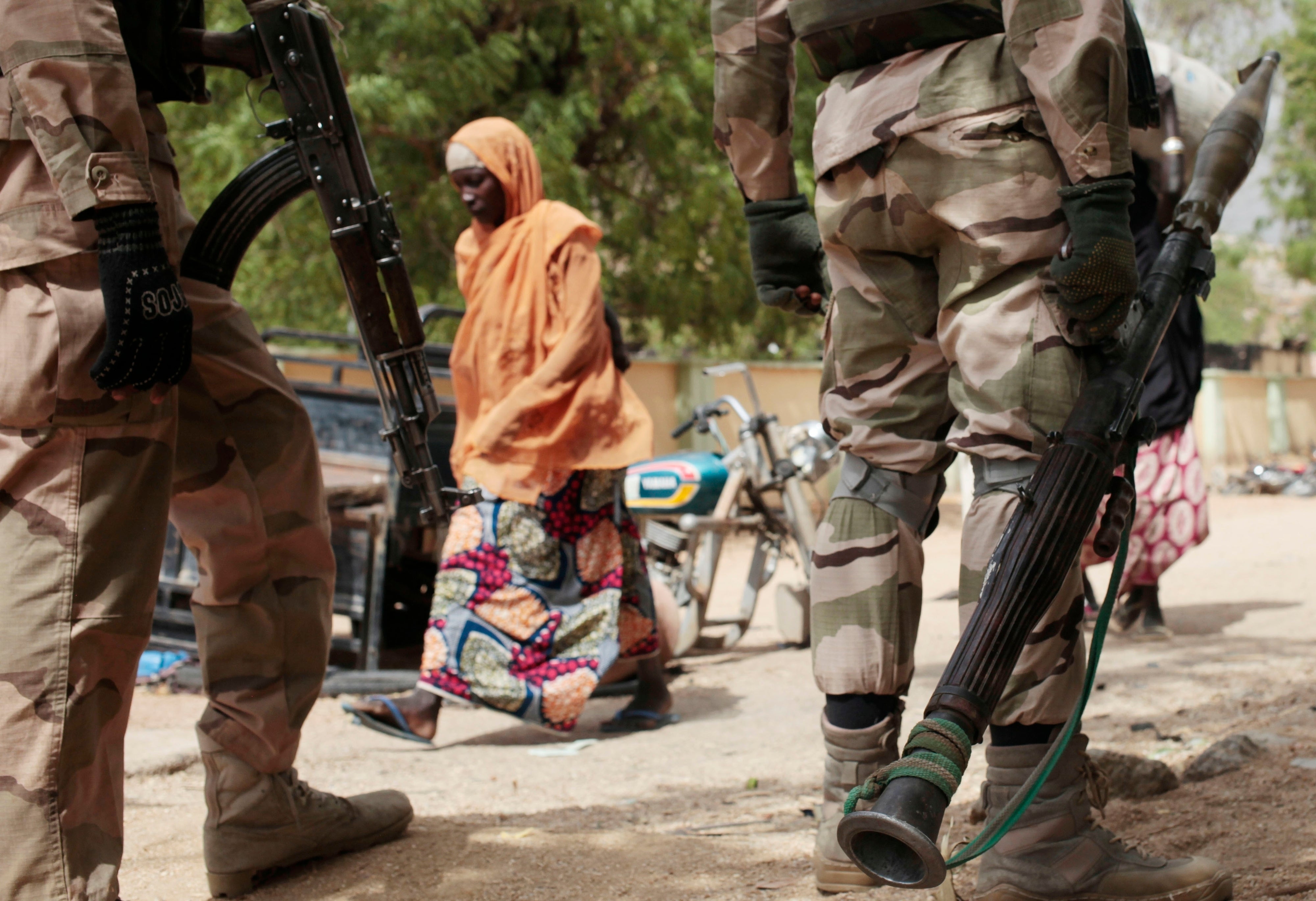 A woman walks past Nigerian soldiers at a checkpoint in Gwoza, northeast, Nigeria, April 8, 2015. (AP Photo/Lekan Oyekanmi, File)
