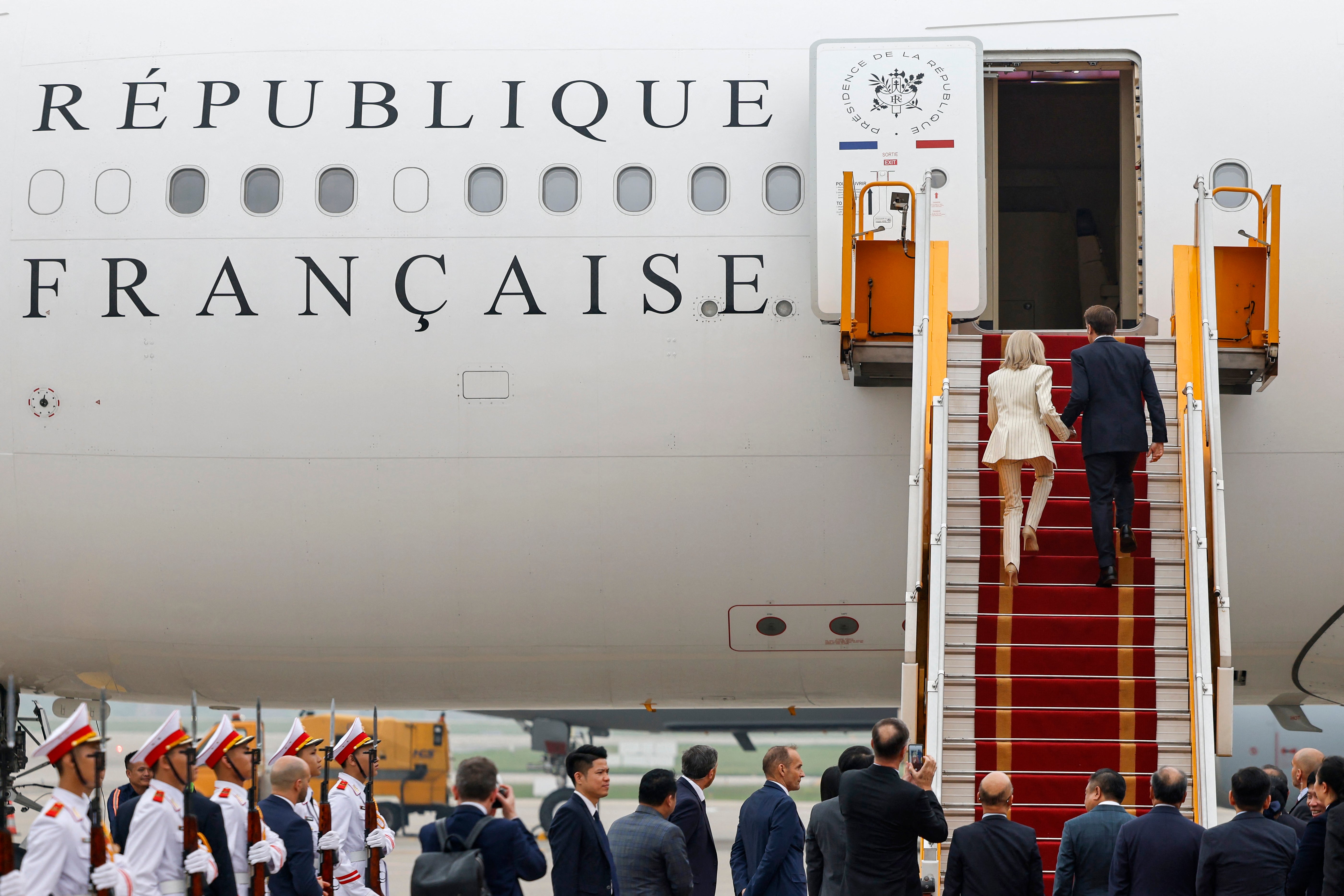 The couple hold hands as the ascend the stairs to France’s presidential plane