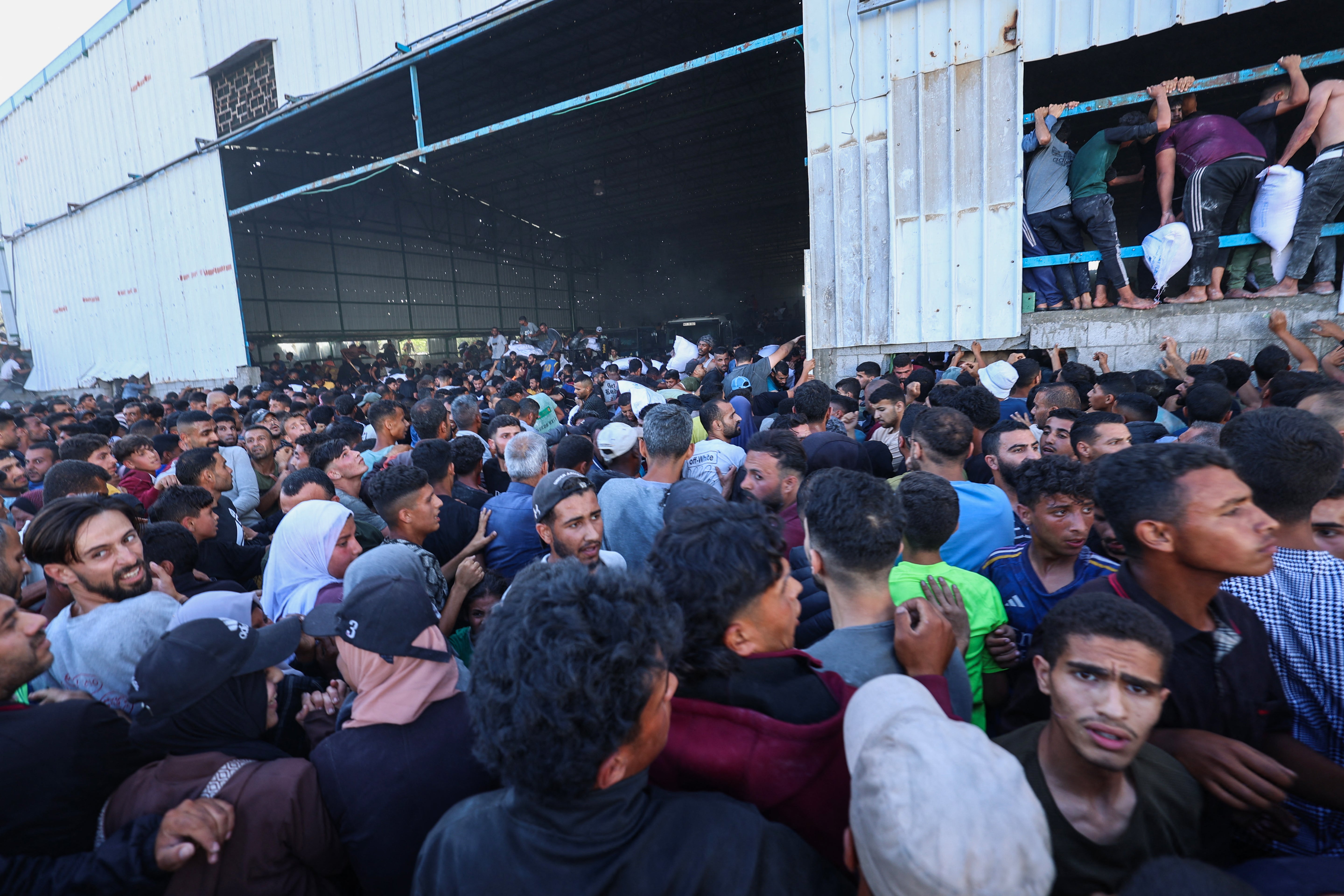 Displaced Palestinians ferry bags of food aid as they storm a World Food Programme warehouse in Deir el-Balah in the central Gaza Strip