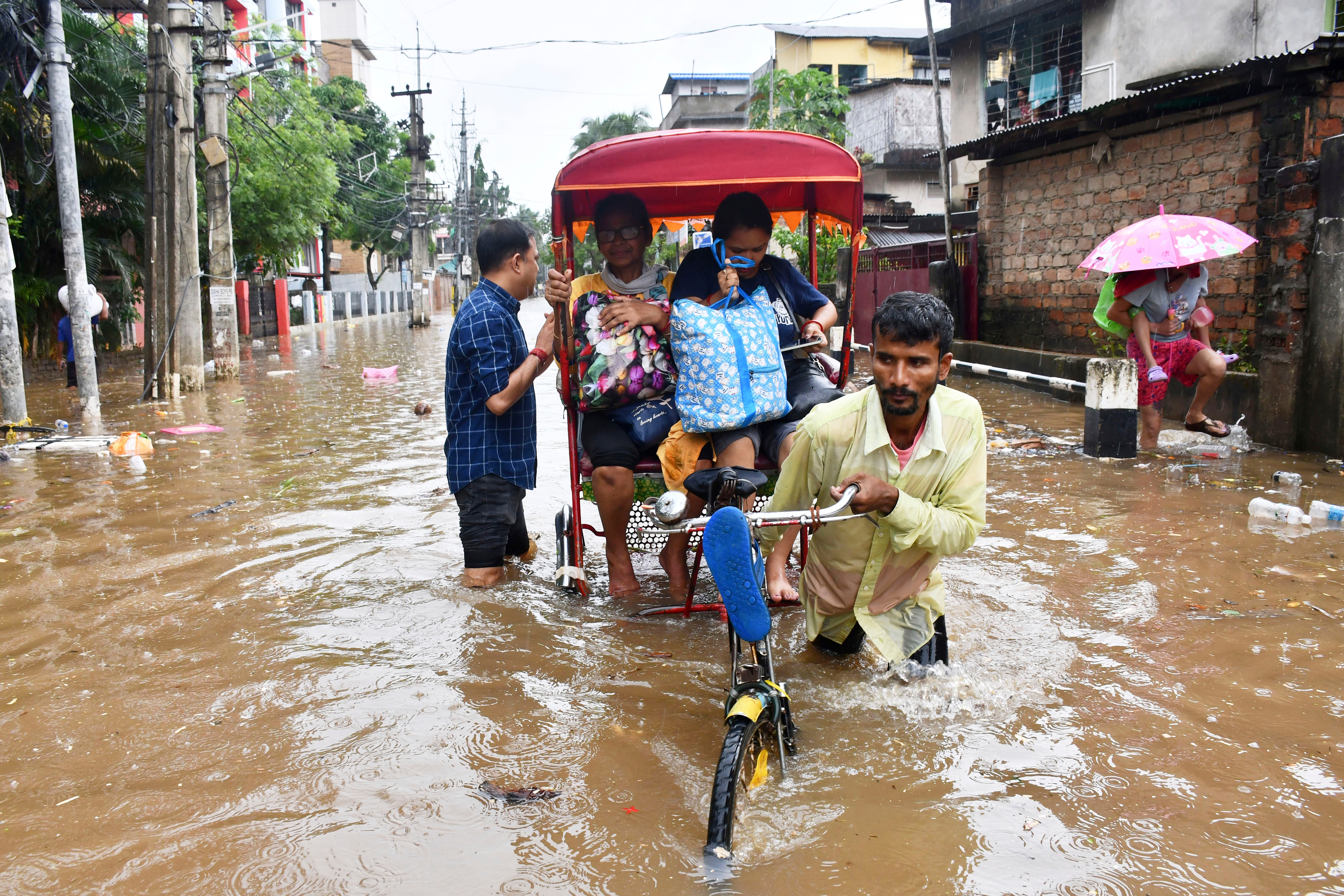 People cross a flooded street on a cycle rickshaw after heavy rains in Guwahati, Assam