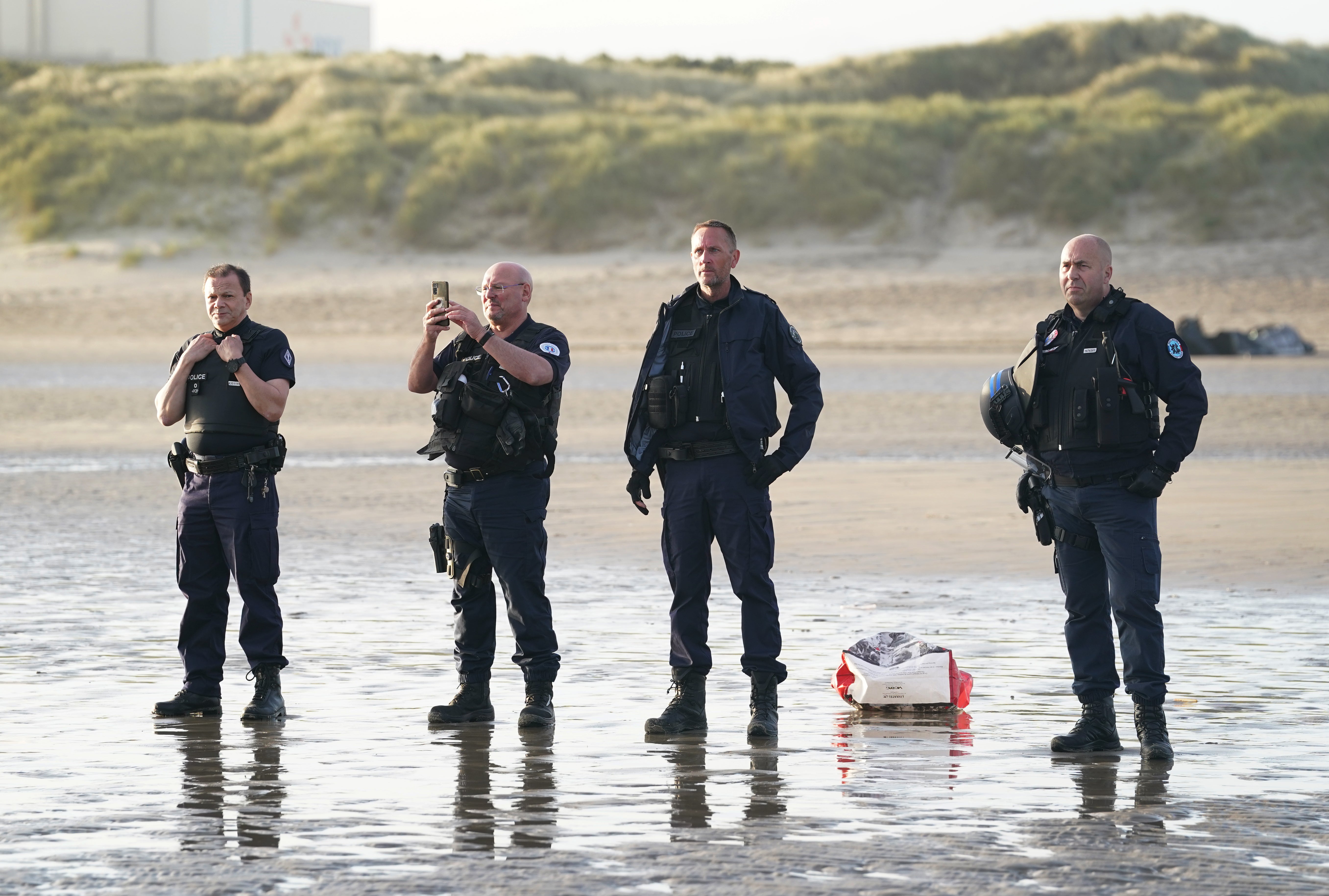 French police officers watch a group of people thought to be migrants board a small boat leaving the beach at Gravelines, France