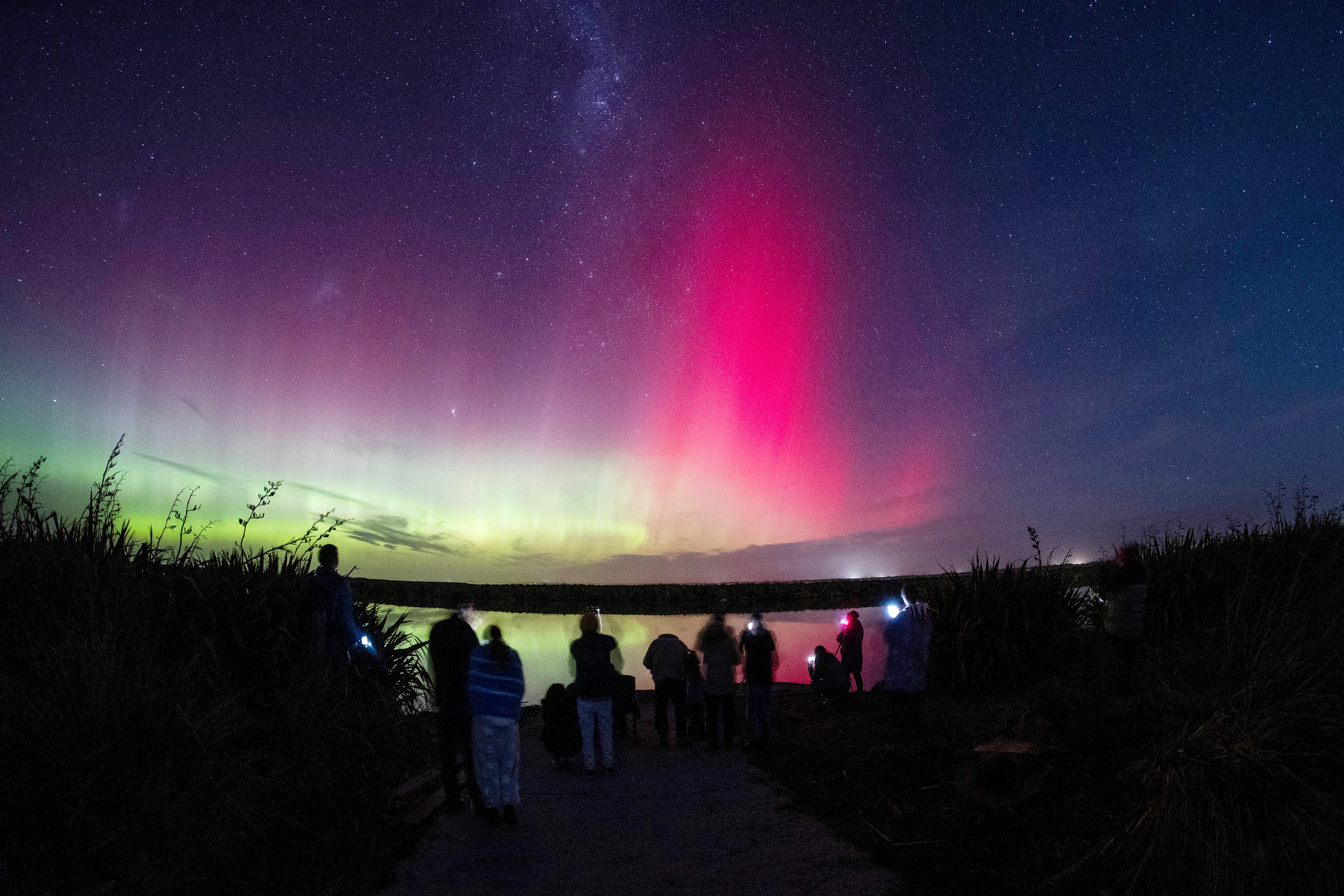 People watch aurora australis, also known as the southern lights, glow on the horizon over Lake Ellesmere on the outskirts of Christchurch