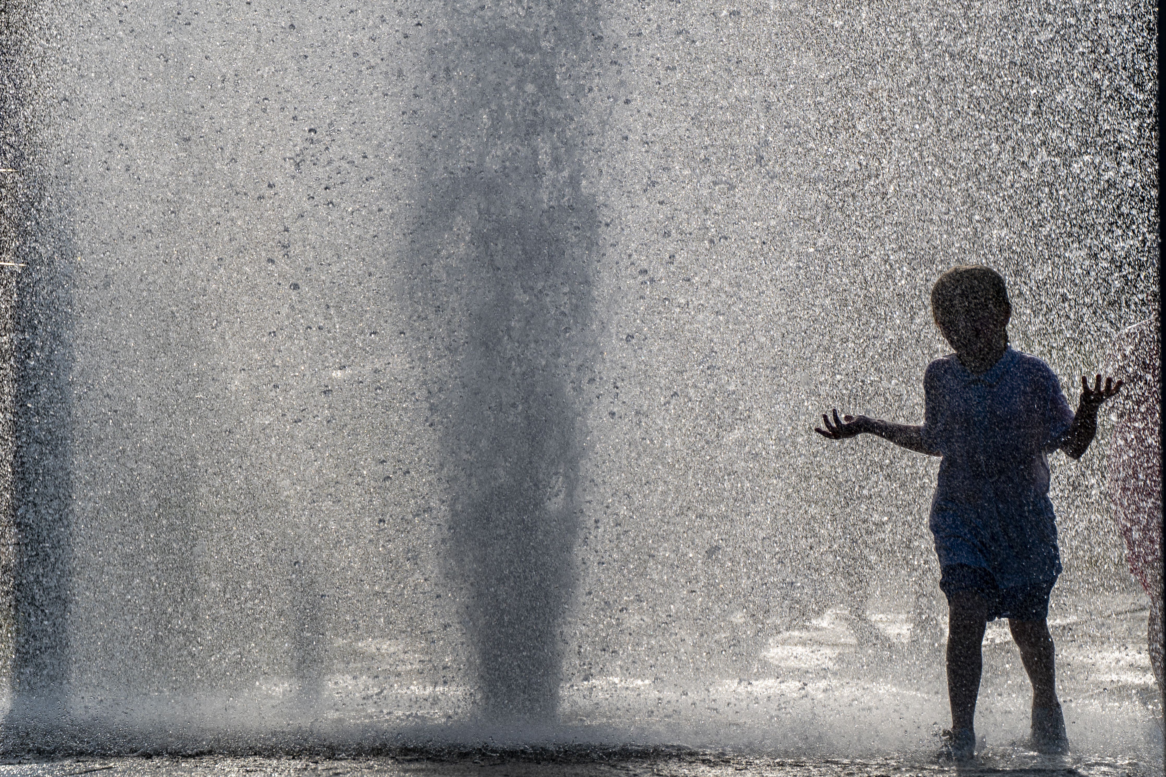 A child plays in a burst water main in Liverpool (PA)