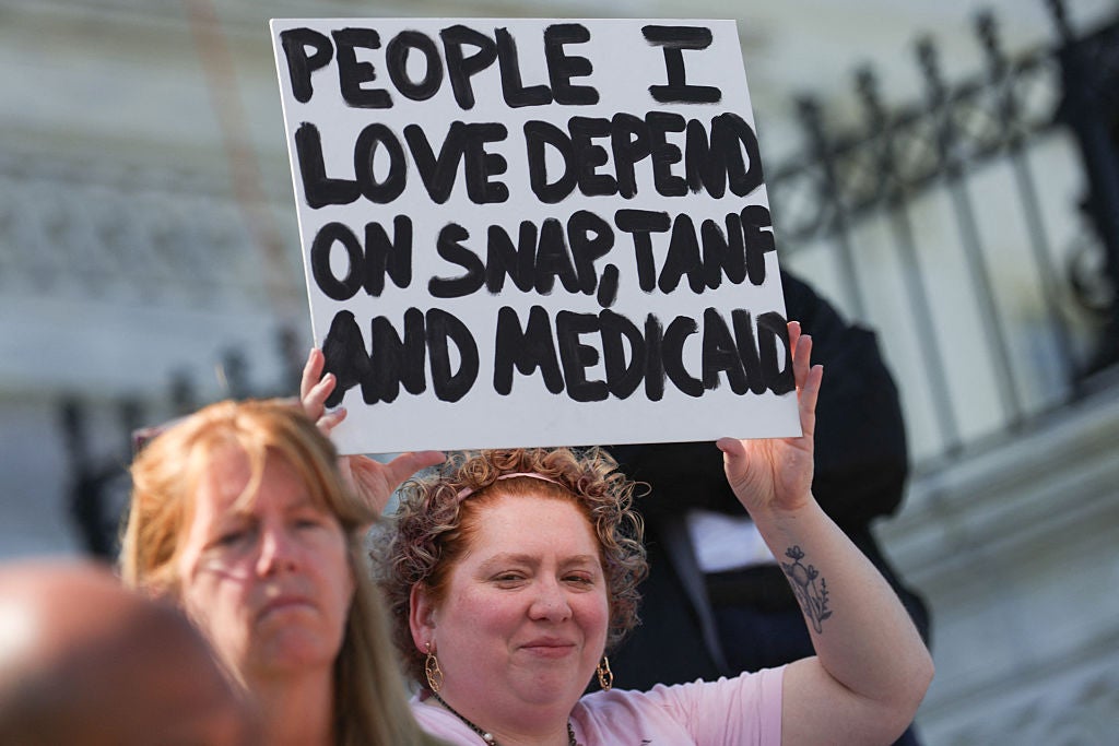 A demonstrator holds a sign with a message against Medicaid cuts on the House steps as House Democratic Leader Hakeem Jeffries speaks to voters