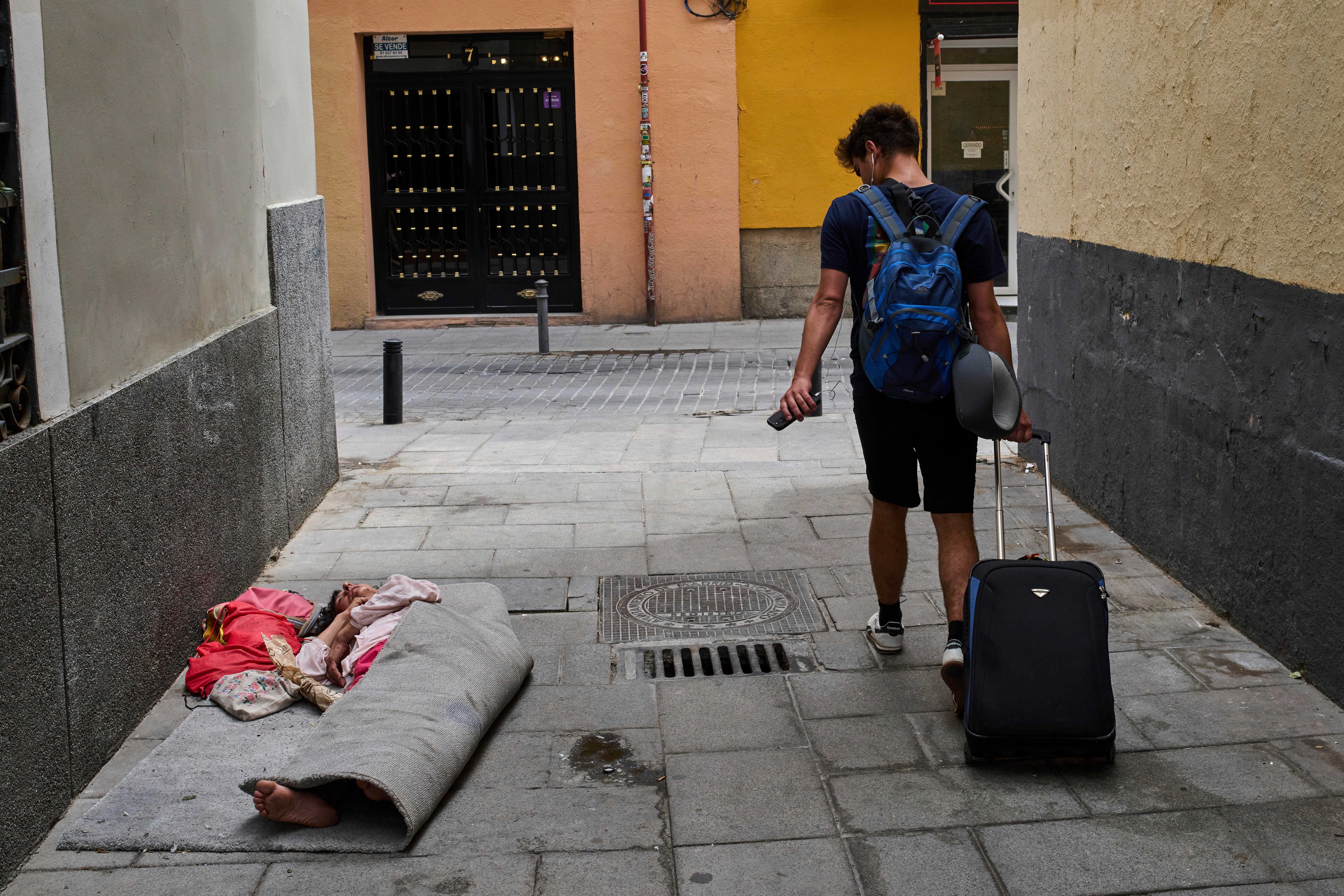 A tourist walks past a homeless woman in downtown Madrid, Spain, Tuesday, June 3, 2025. (AP Photo/Bernat Armangue)