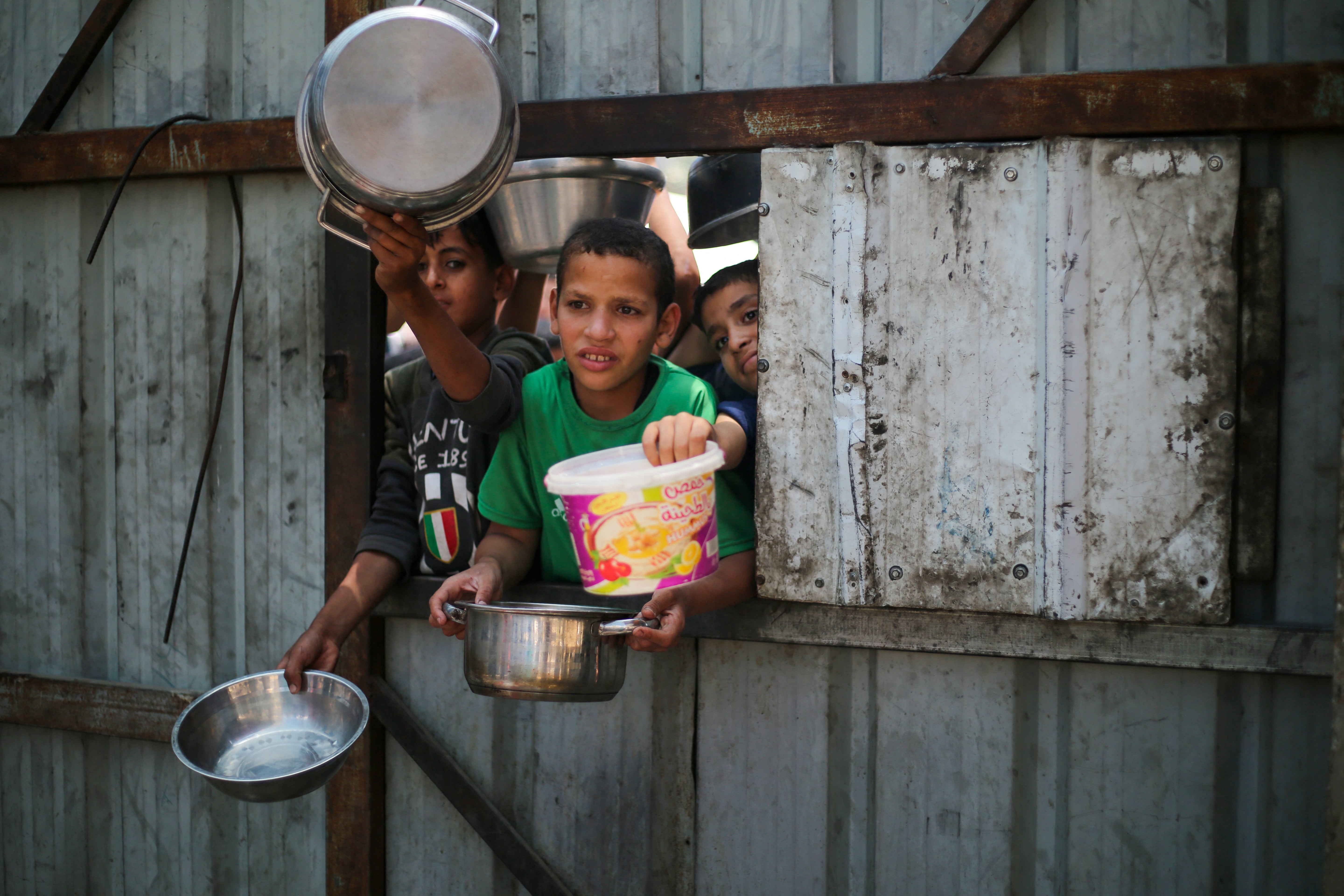 Palestinian children reach out with their pots as they wait for food at a distribution point in Nuseirat, central Gaza Strip