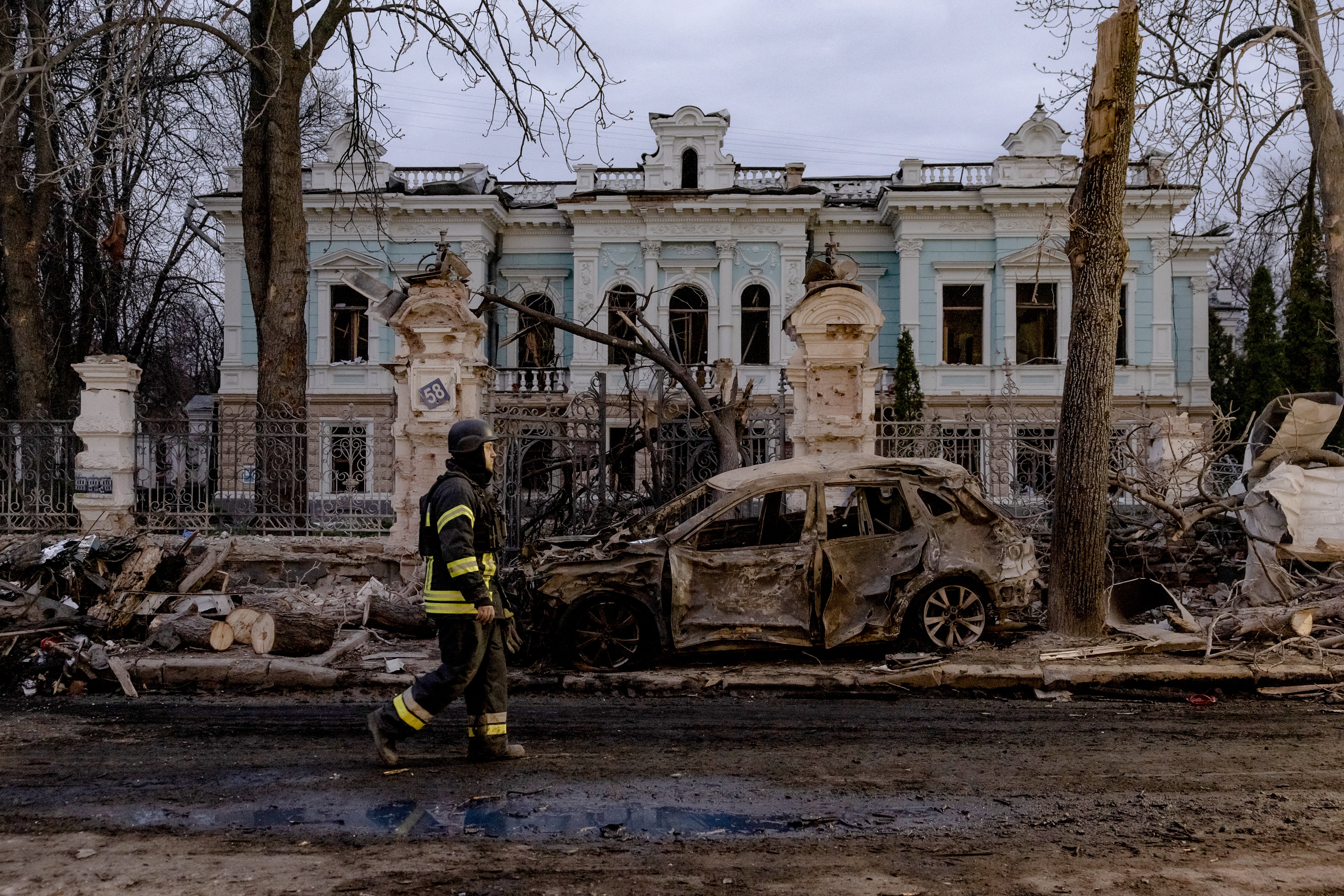 A Ukrainian rescuer walks by a burned car in front of damaged building at the site of a missile attack in Sumy, northeastern Ukraine, on April 13, 2025