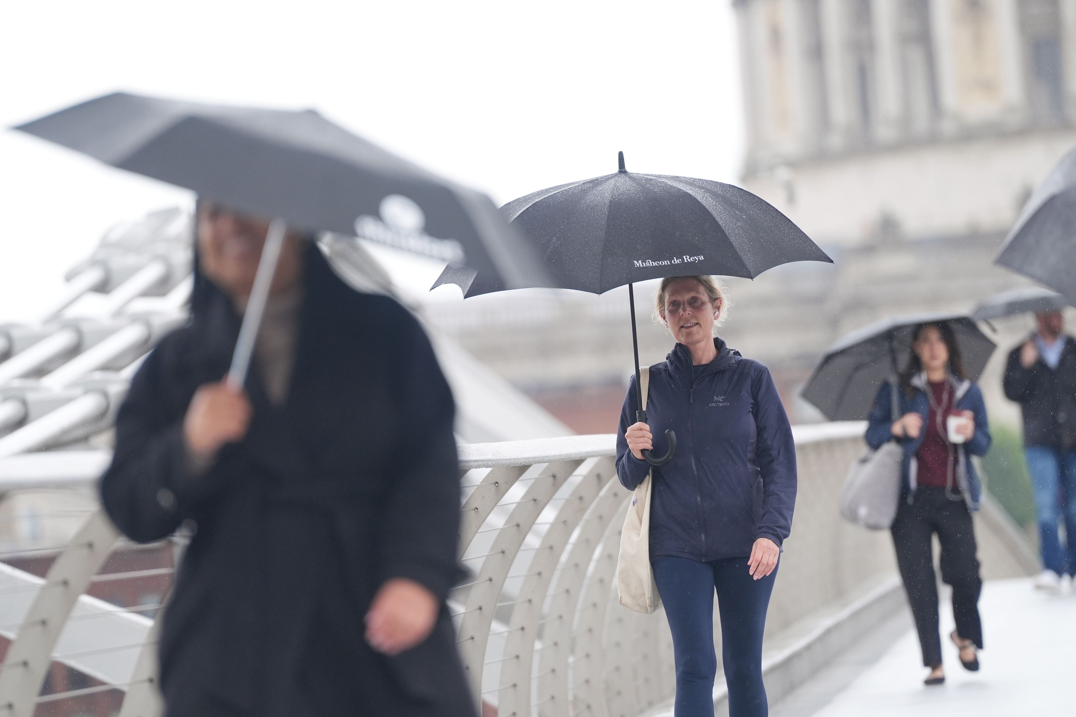 People with umbrellas walk along the Millennium Bridge, in London, during a rain shower (Yui Mok/PA)