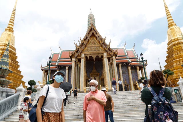 <p>People wear masks at Temple of the Emerald Buddha in Bangkok, Thailand</p>