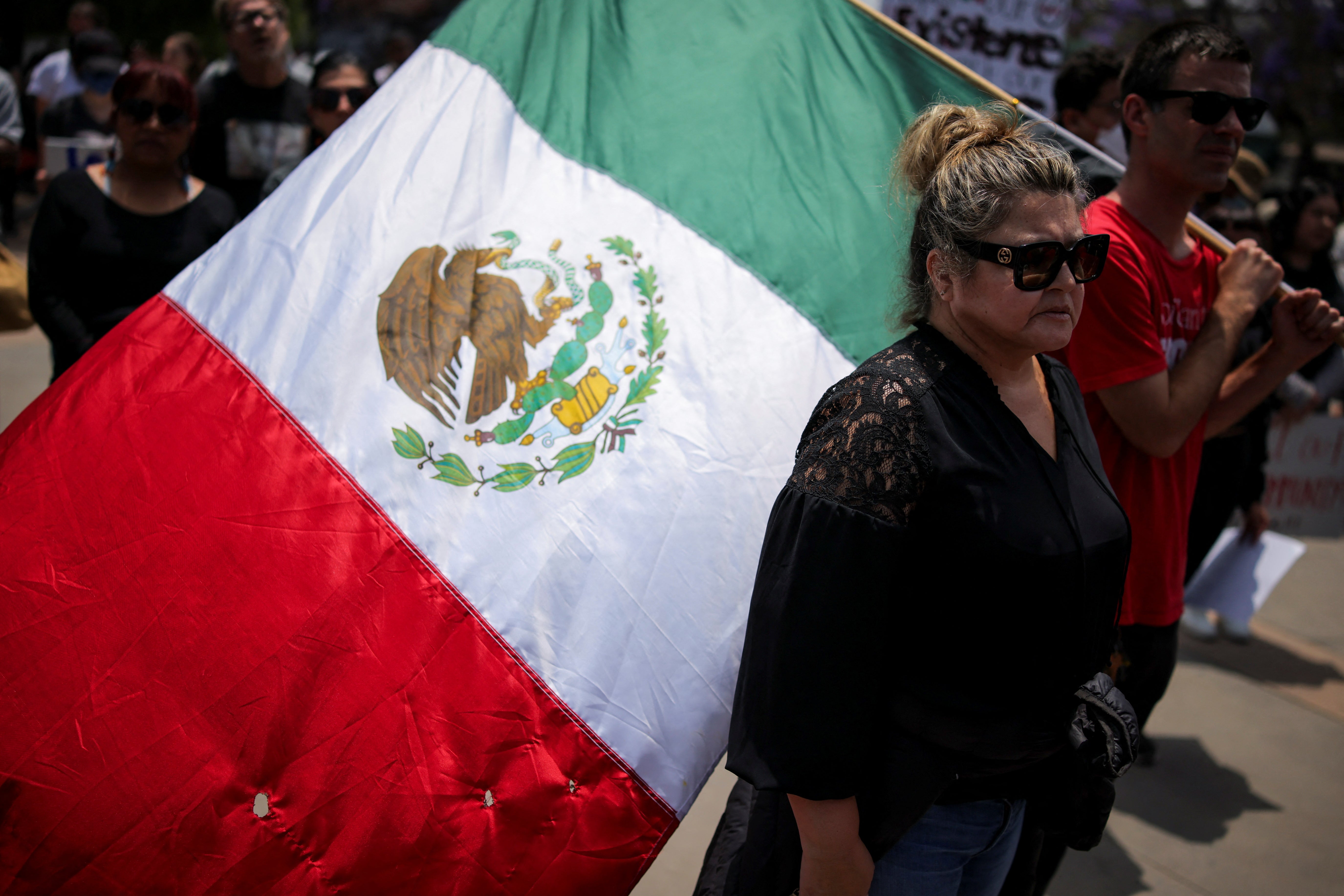 A woman stands next to a man carrying a Mexican flag, at a protest against federal immigration sweeps in the Boyle Heights neighborhood of Los Angeles, California on June 8