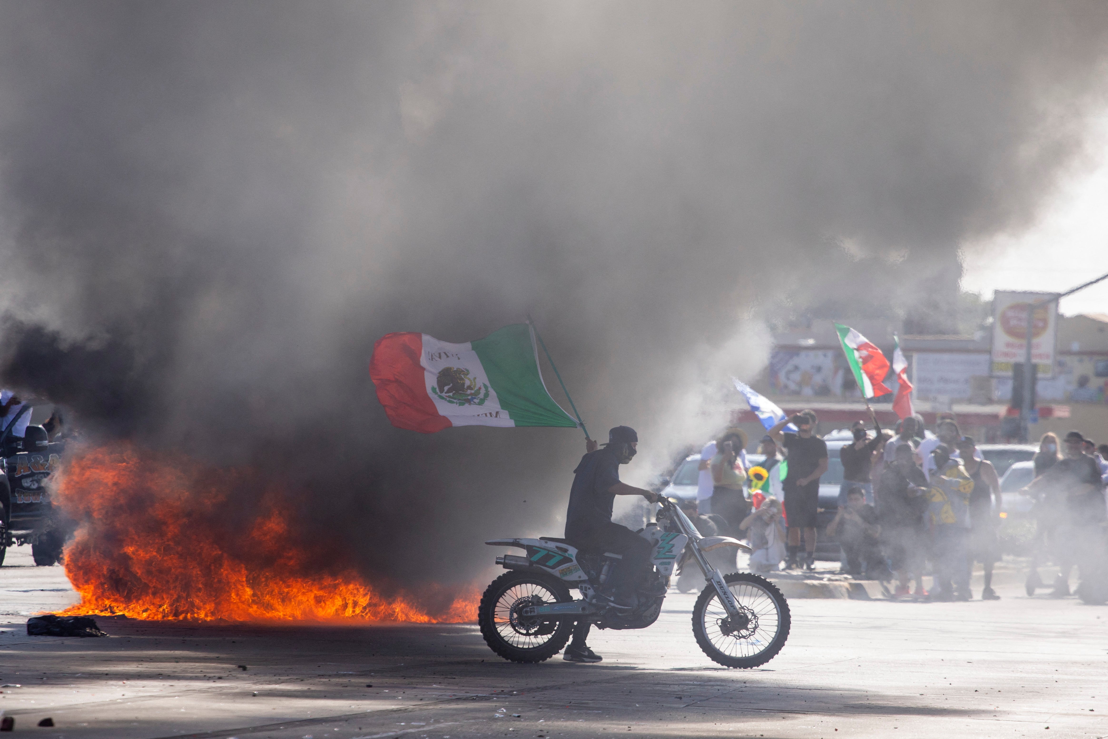 A demonstrator waving a Mexican national flag next to a car on fire in L.A.’s Compton neighborhood