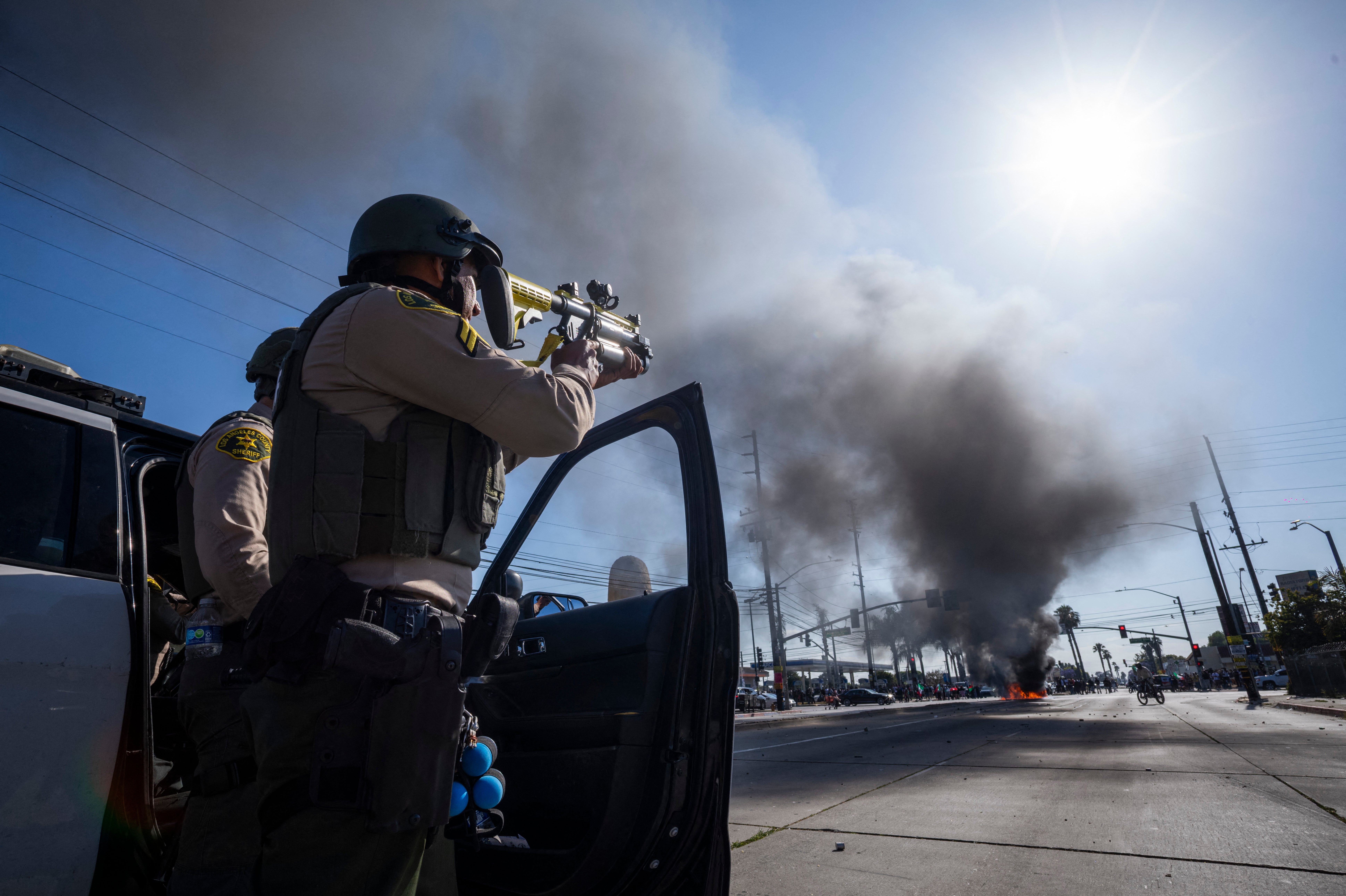 A law enforcement officer aims his firearm close to the site of a burning vehicle in the Compton neighborhood of Los Angeles