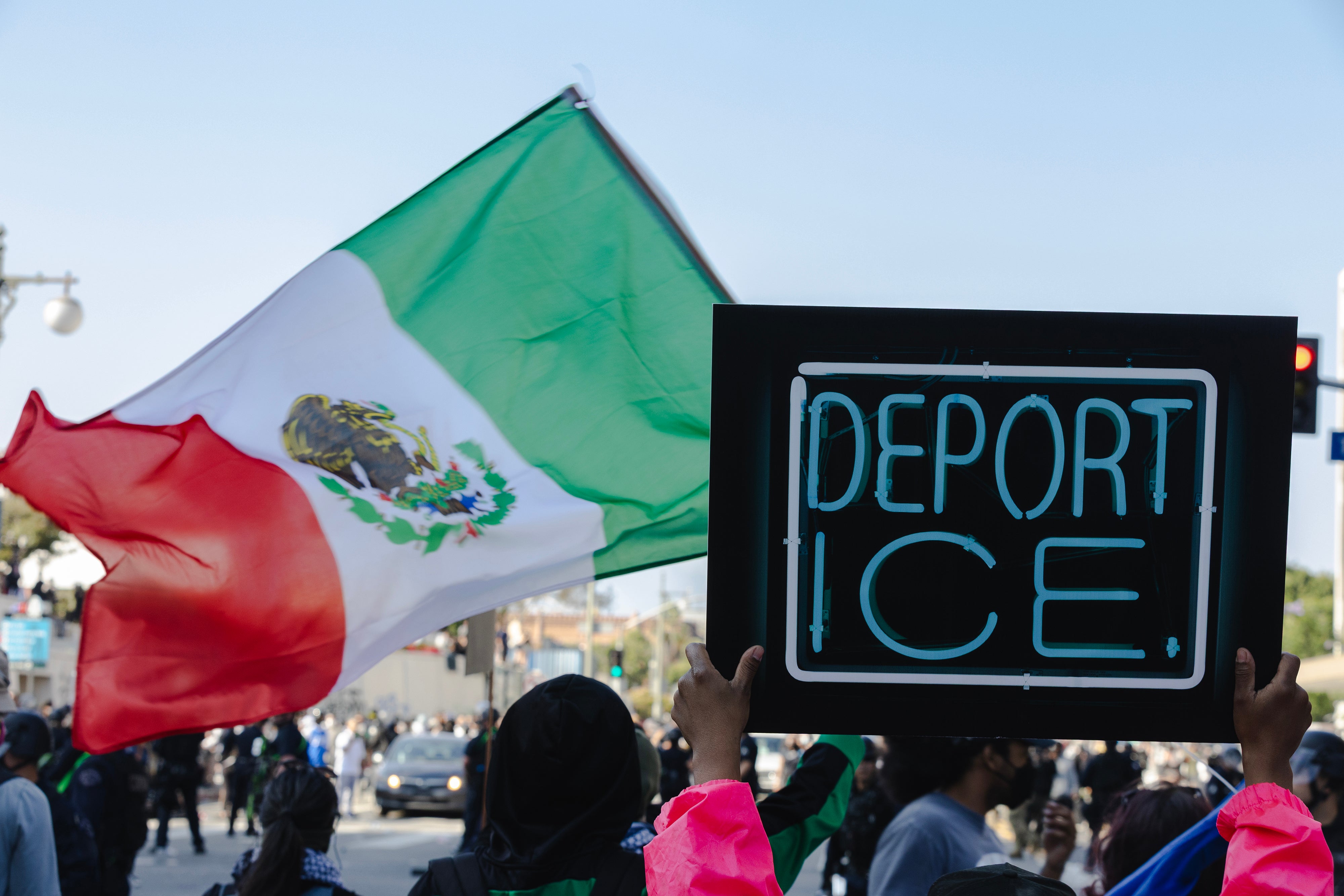 Protesters hold anti-ICE signs and a Mexican flag during clashes between police and demonstrators