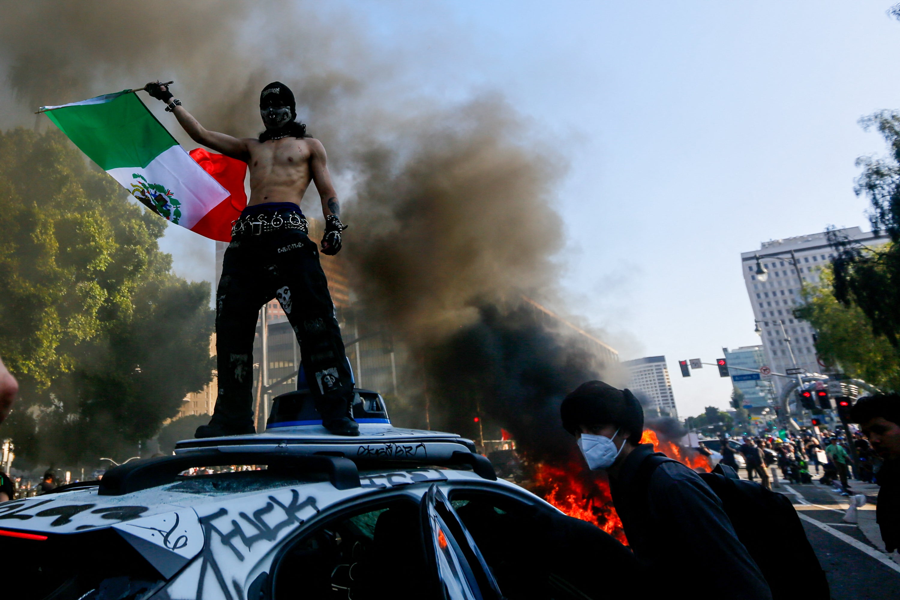 A protester waves the Mexican flag atop a Waymo vehicle during an anti-ICE protest in downtown Los Angeles