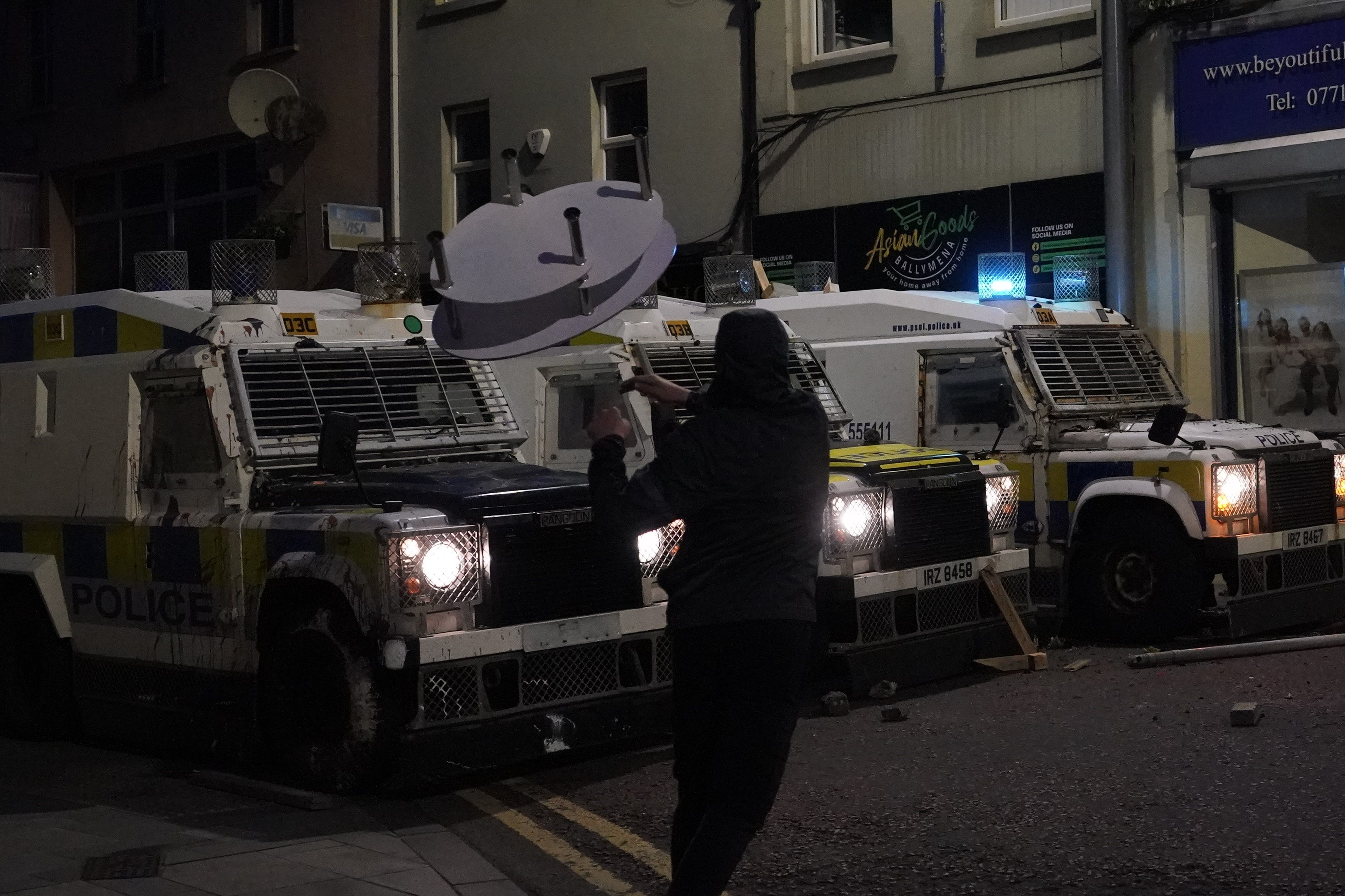 A demonstrator throws a glass table at PSNI vehicles during violence in Ballymena on Tuesday (Niall Carson/PA)