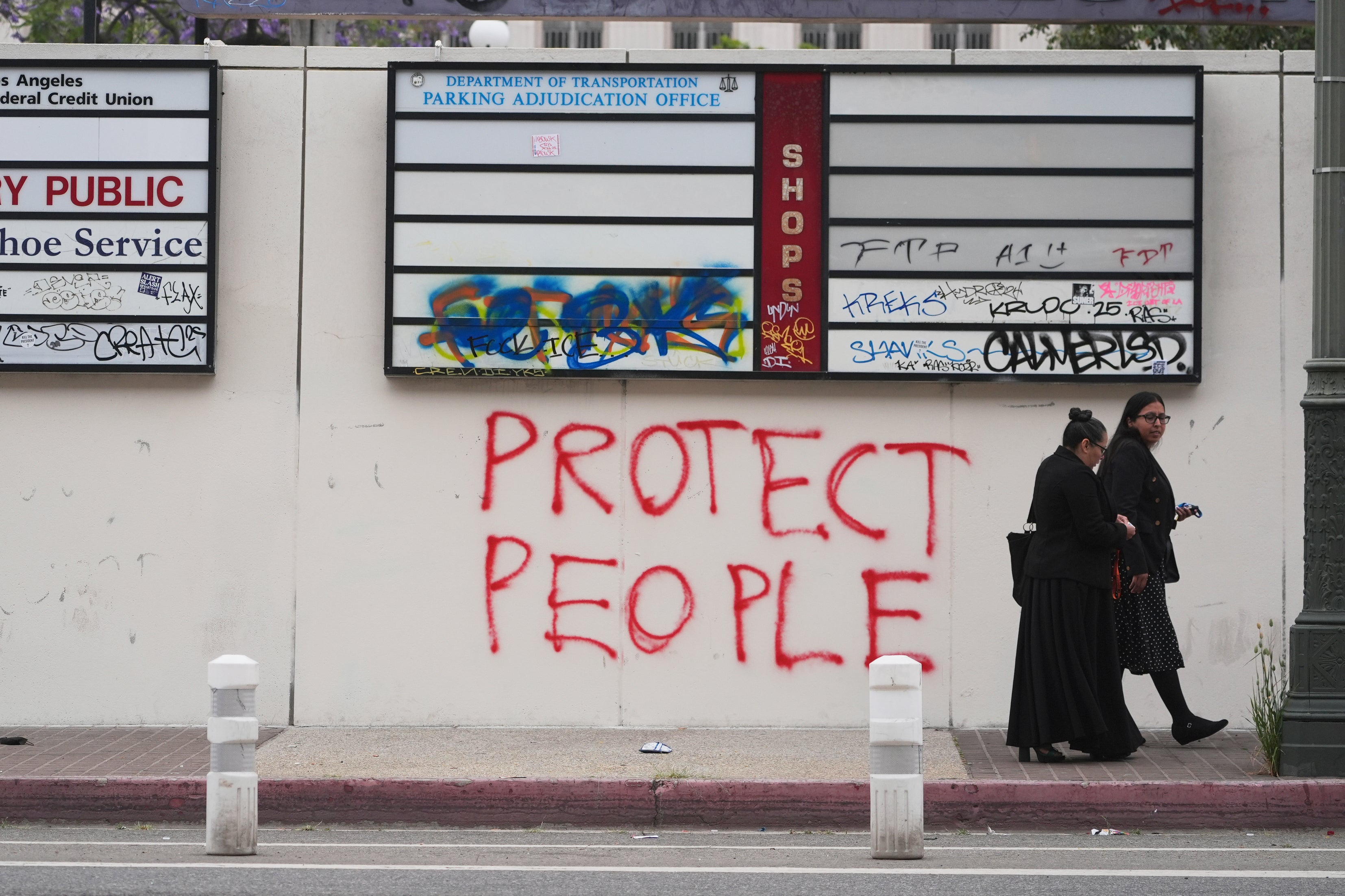 People walk past graffiti from recent protests against federal immigration raids in LA