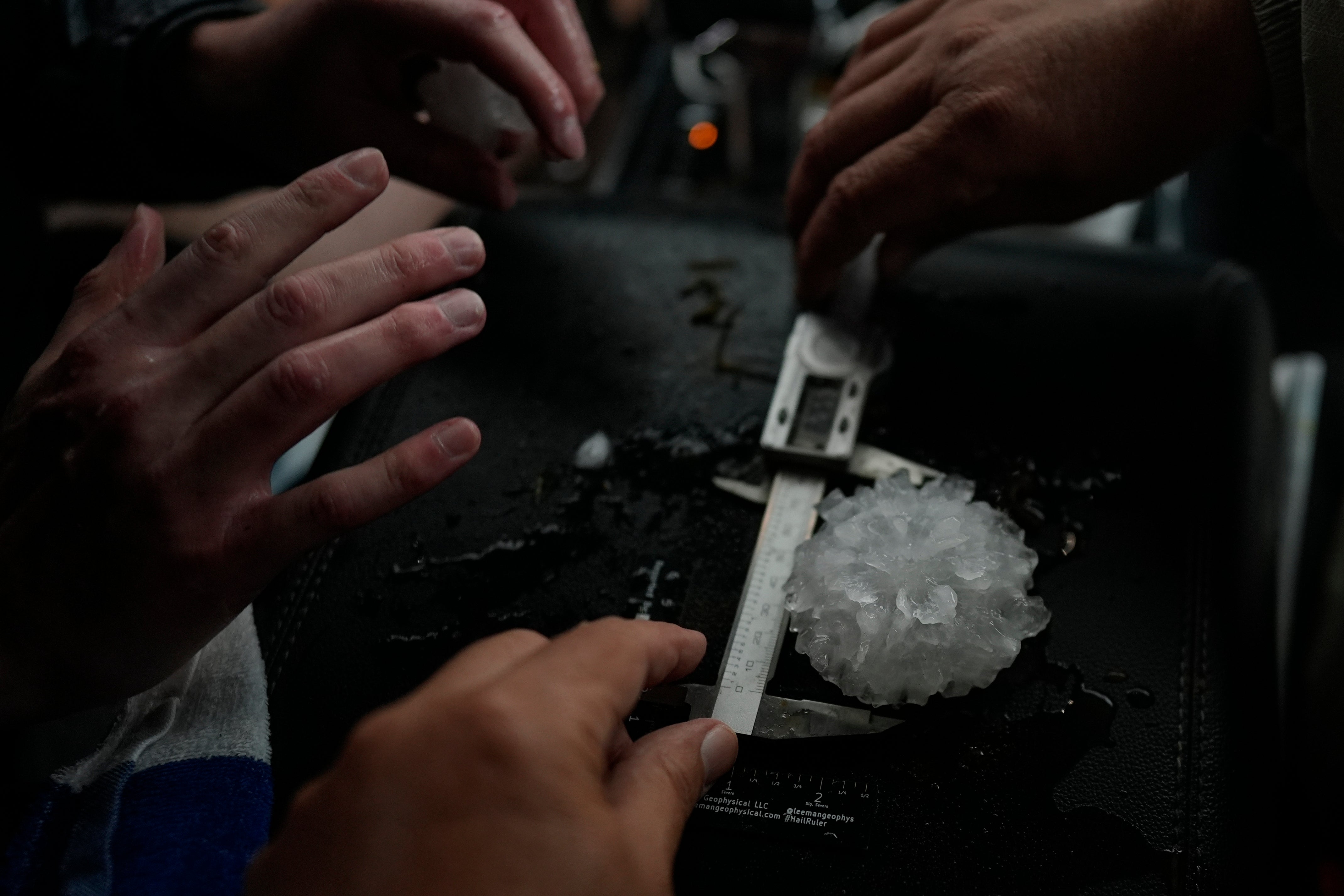 Tony Illenden, left, and Tim Marshall measure a large hail shaped like a rose between the front seats of Northern Illinois University's Husky Hail Hunter vehicle during a Project ICECHIP operation Friday, June 6, 2025, in Morton, Texas. (AP Photo/Carolyn Kaster)