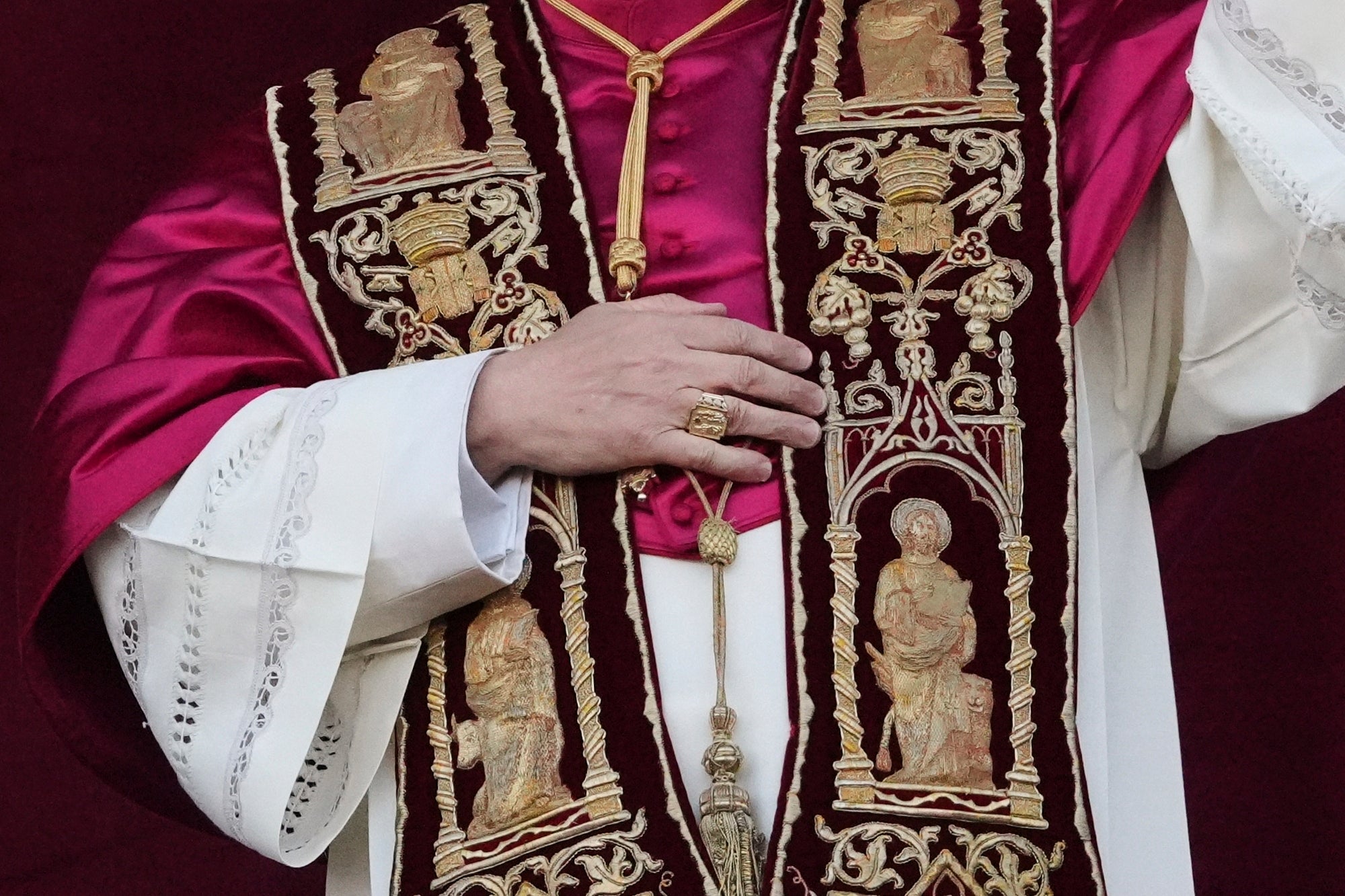 He wore a red satin mozzetta shoulder cape, the burgundy stola with gold embroidery and a gold cross held by a double-stranded silken gold cord