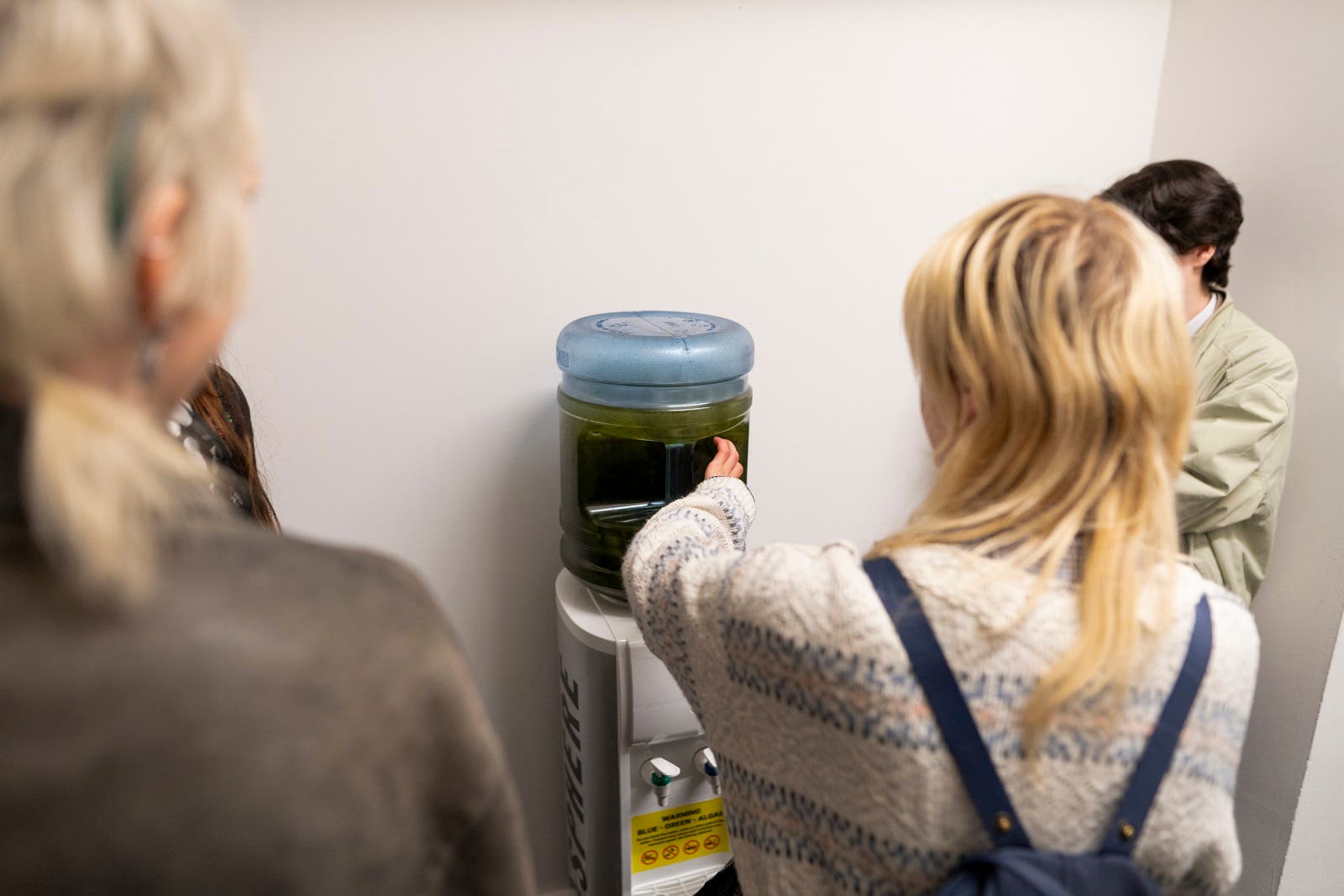 As Belfast Photo Festival 2025 launches, the team are prominently displaying images of Lough Neagh’s Toxic Blue Green Algal on digital billboards across the city, to recognise the fragility, immediacy and urgency of the exhibitions on Natural Heritage. Small algal blooms are already appearing around the Lough and will soon – yet again – cause the widespread danger, disruption and dismay experienced in previous years. Furthermore, to capture and share up close how so many of the underlying causes of this complex issue remain unchecked The team have also installed 3 deactivated water coolers at Botanic Gardens, the Ulster Museum and Belfast Exposed, filled and sealed with water from the Lough’s environment, including algae from the Lough, slurry scum from its tributaries and the outflow water from an industrial area. The water coolers are deactivated and branded with a public warning sticker as used by the public authorities. They give the public a chance to get up close to the same pollution and effluent that is pouring into a natural treasure and the source of over 40% of Northern Ireland’s drinking water. (Belfast Photo Festival)